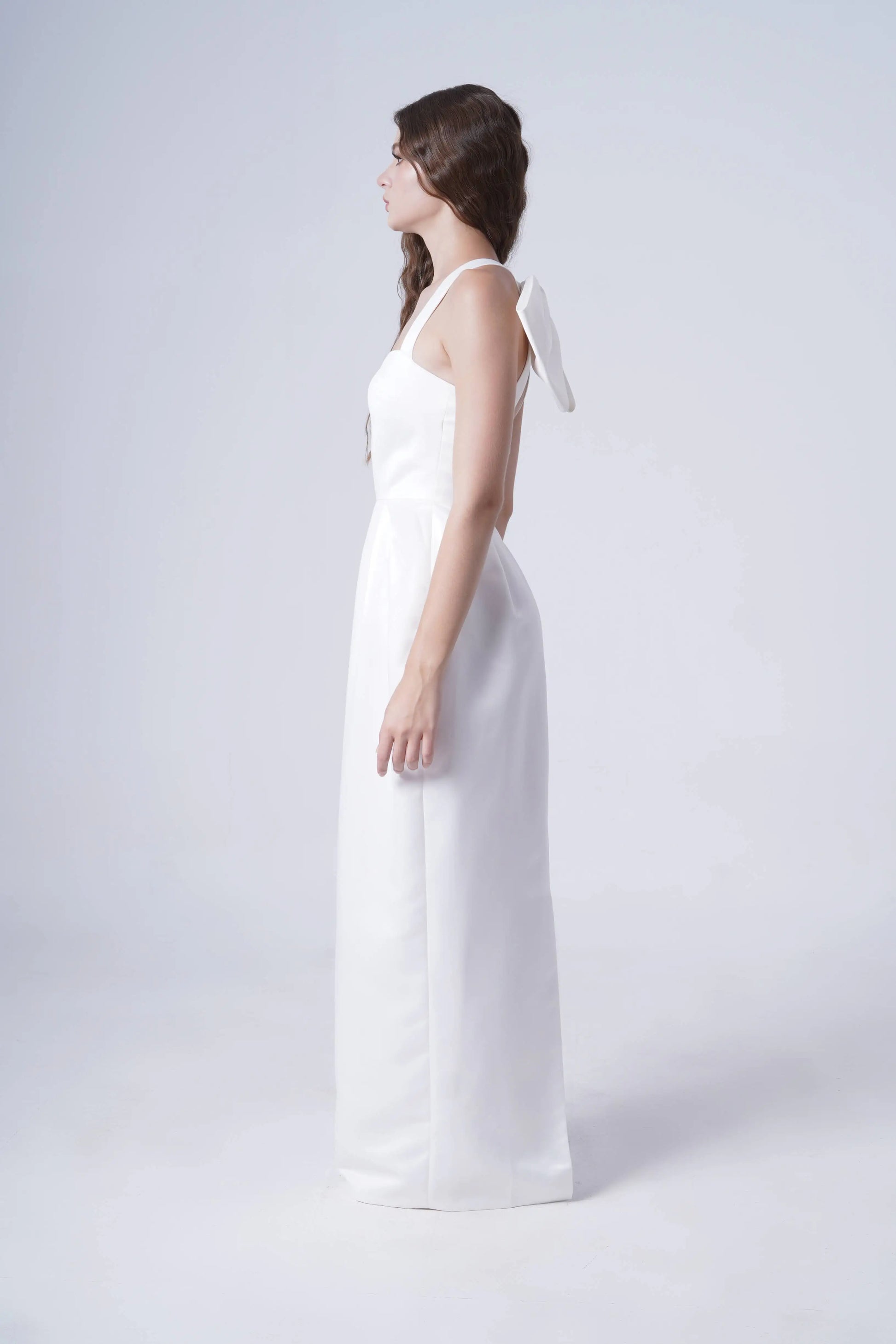 Woman wearing a white dress with thin straps on a plain background