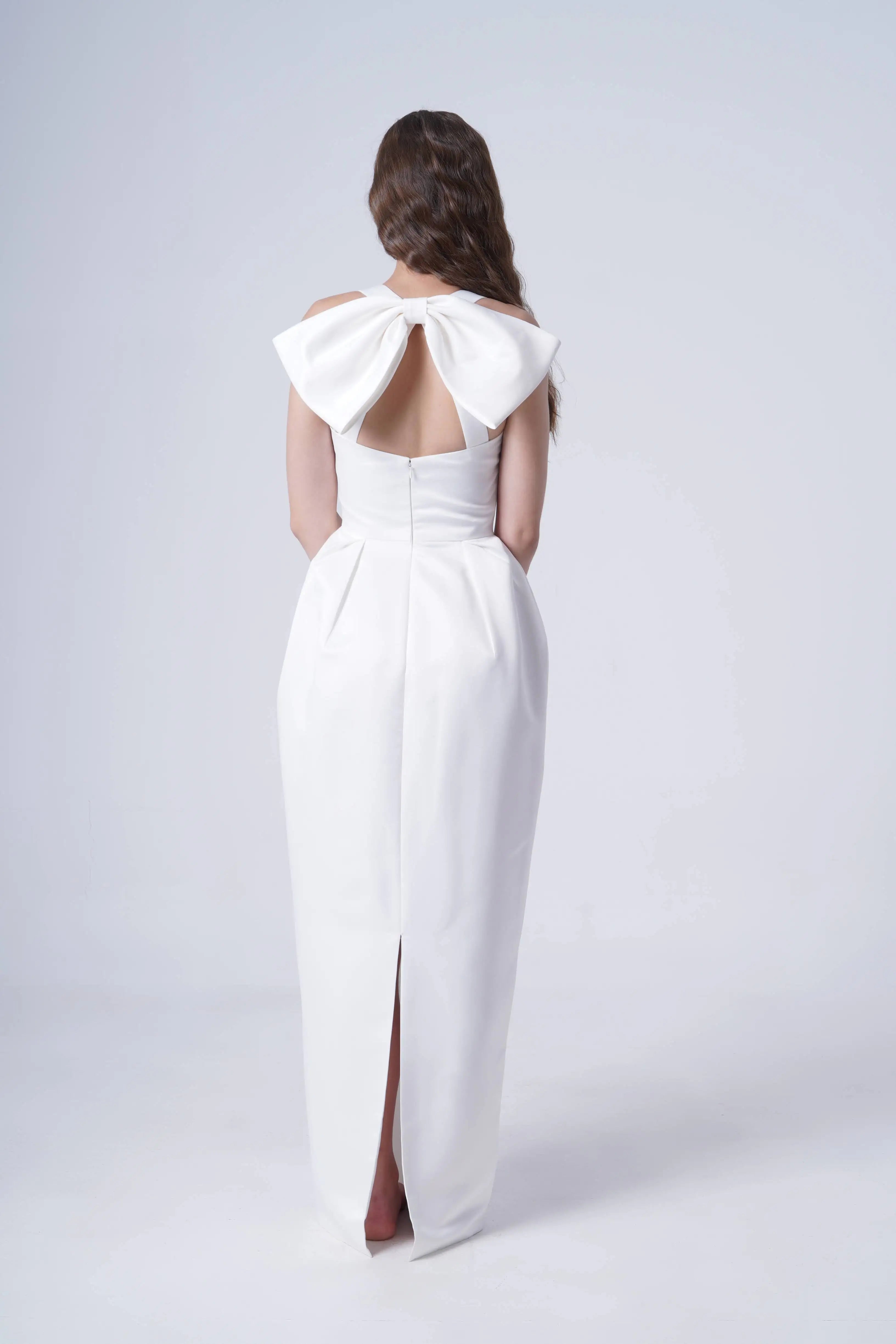 Woman wearing a white evening gown with a large bow at the back on a light gray background