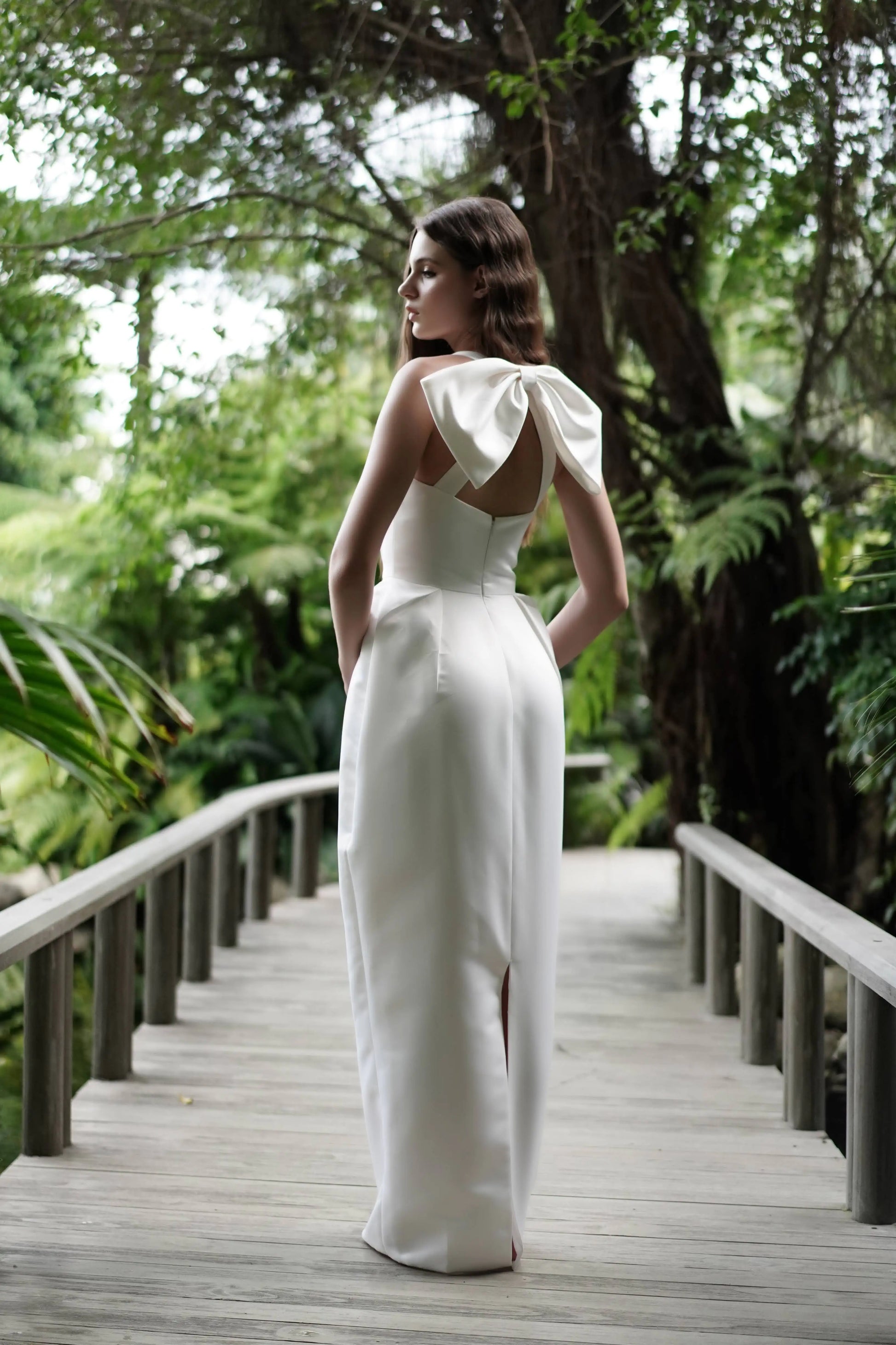 Woman in a white dress standing on a wooden bridge in a forest setting