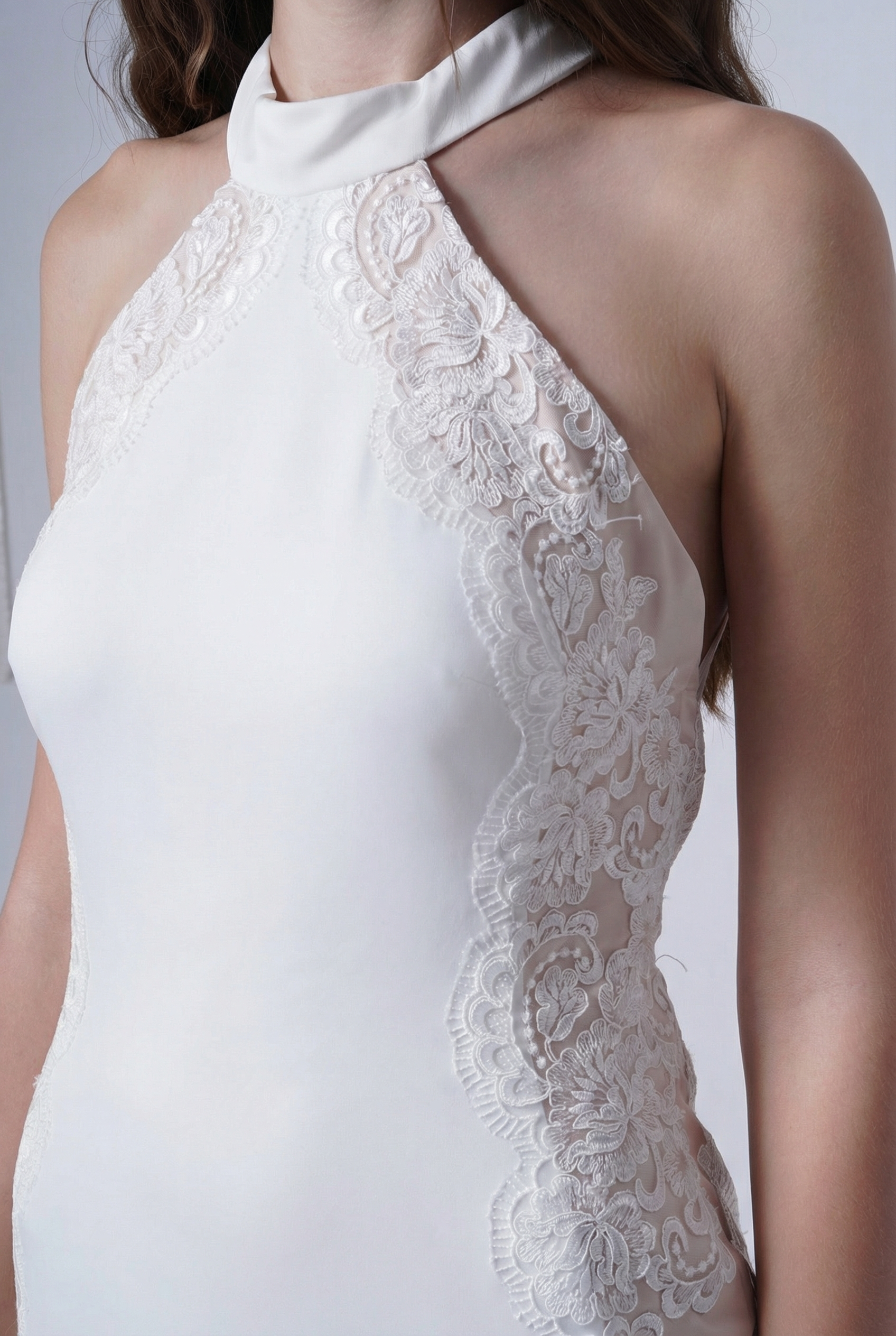 A woman wears the Luisa Bridal Dress in Ivory by TH&TH, a sleeveless satin gown featuring lace side detailing and a halter neckline, shown from the shoulders to the waist.