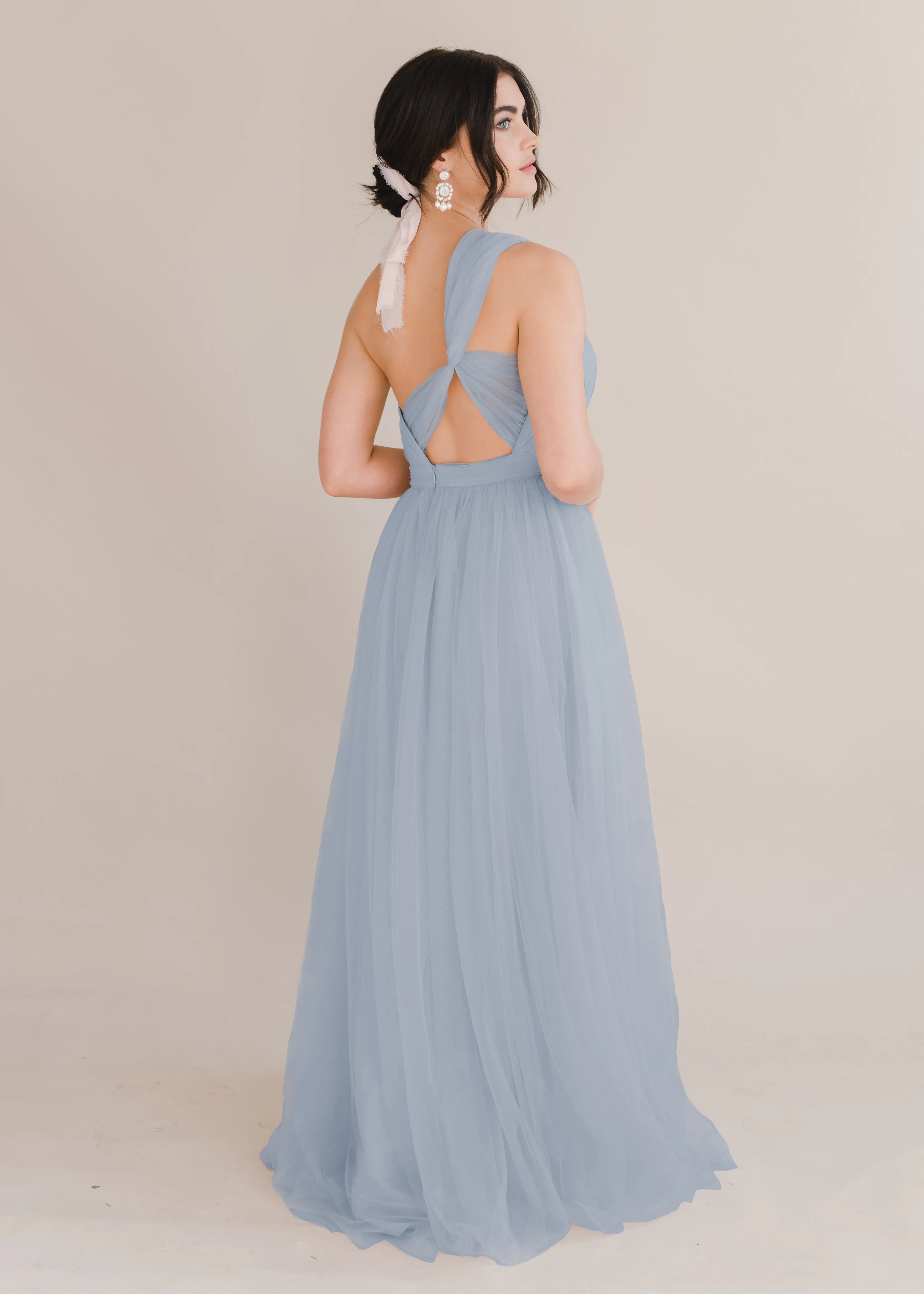 A woman wearing a dusty blue bridesmaid dress with one shoulder strap on a white background by TH&TH Bridesmaids. 
