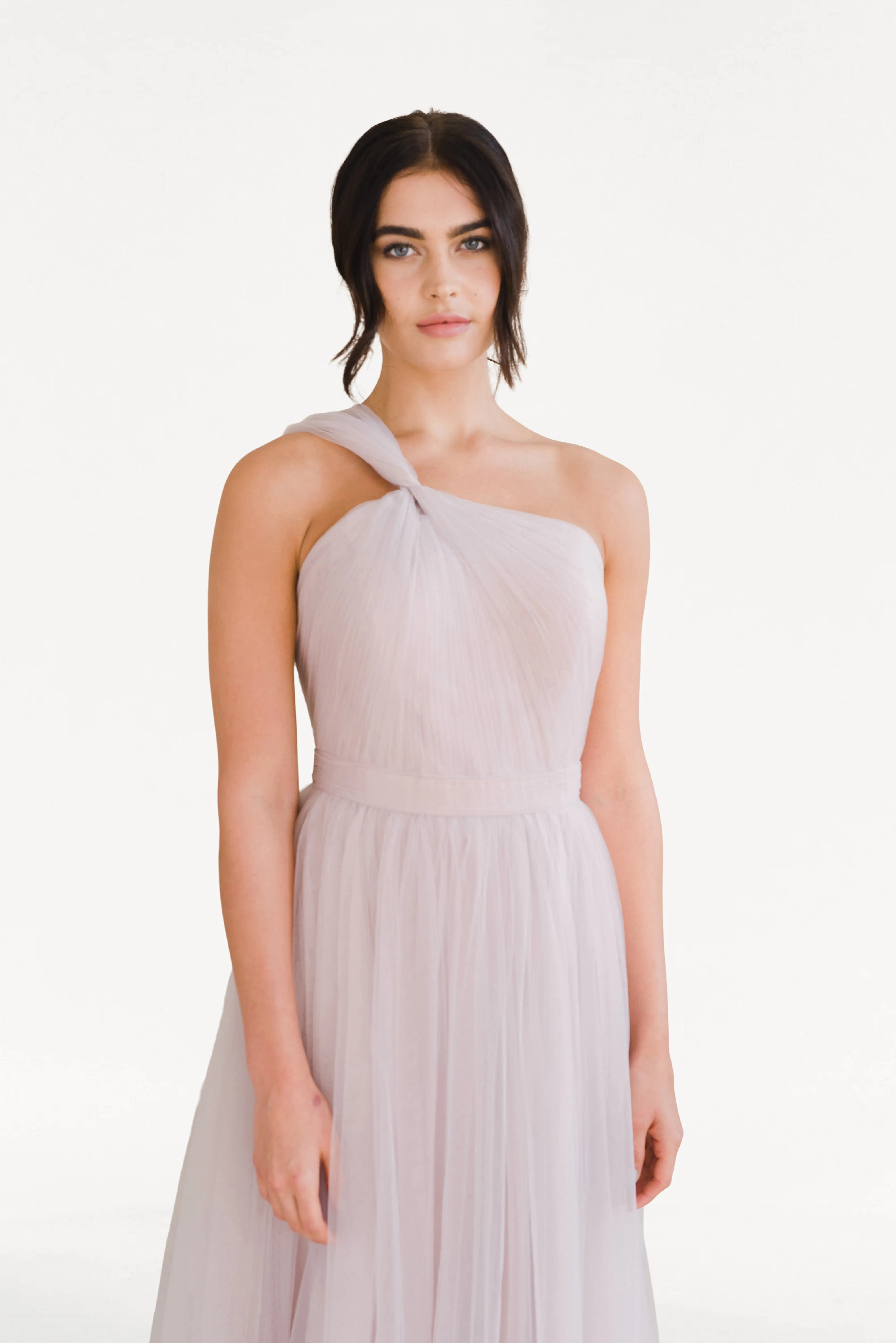 A woman with dark wavy hair wears the TH&TH Luna Bridesmaid Dress in Smoked Blush Tulle, standing facing forward against a plain white background and looking calmly at the camera.
