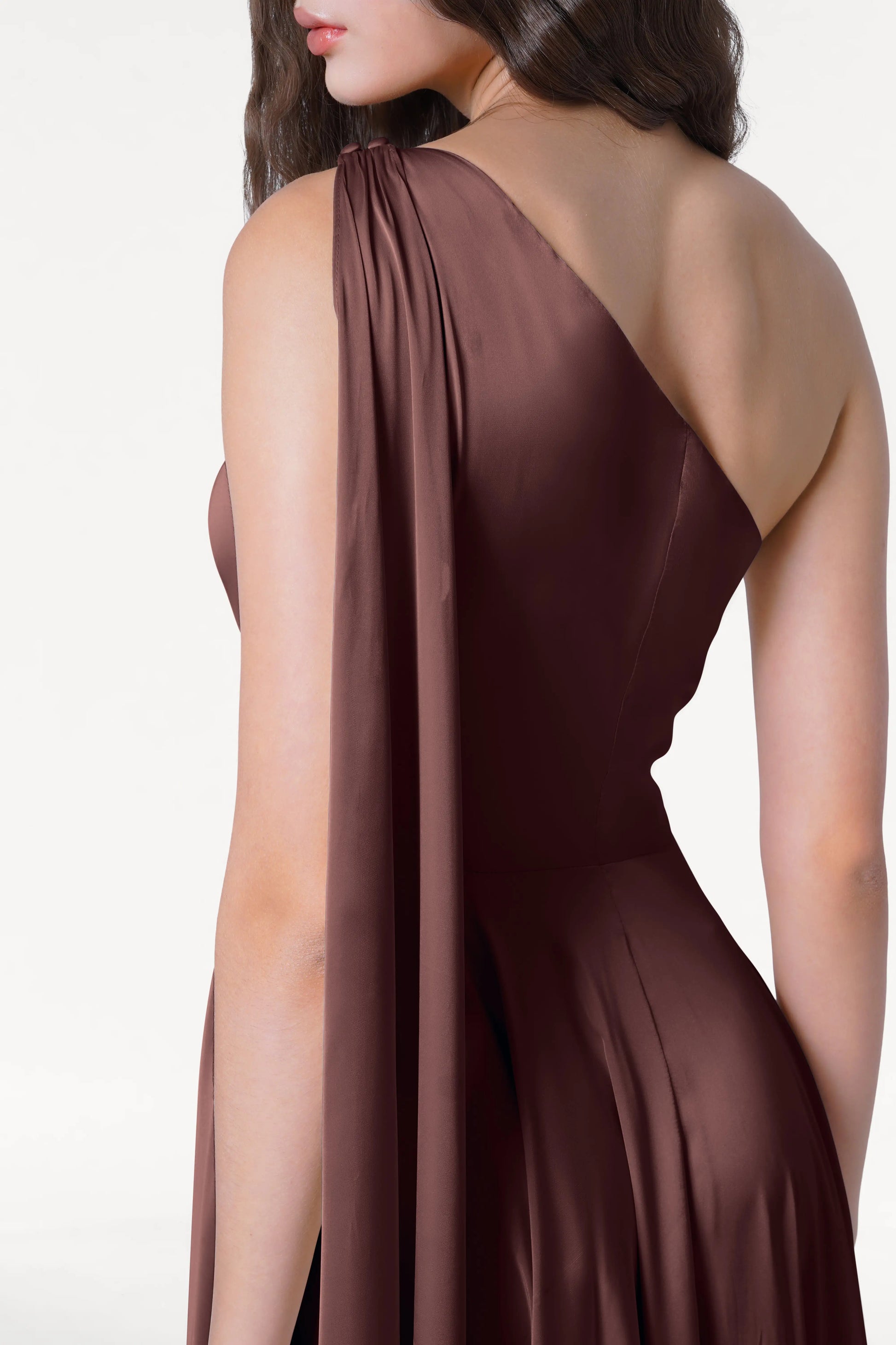 A woman models the TH&TH Lyra Bridesmaid Dress in Chocolate Brown Satin against a white background, her face partially hidden and wavy hair elegantly draped over one shoulder.