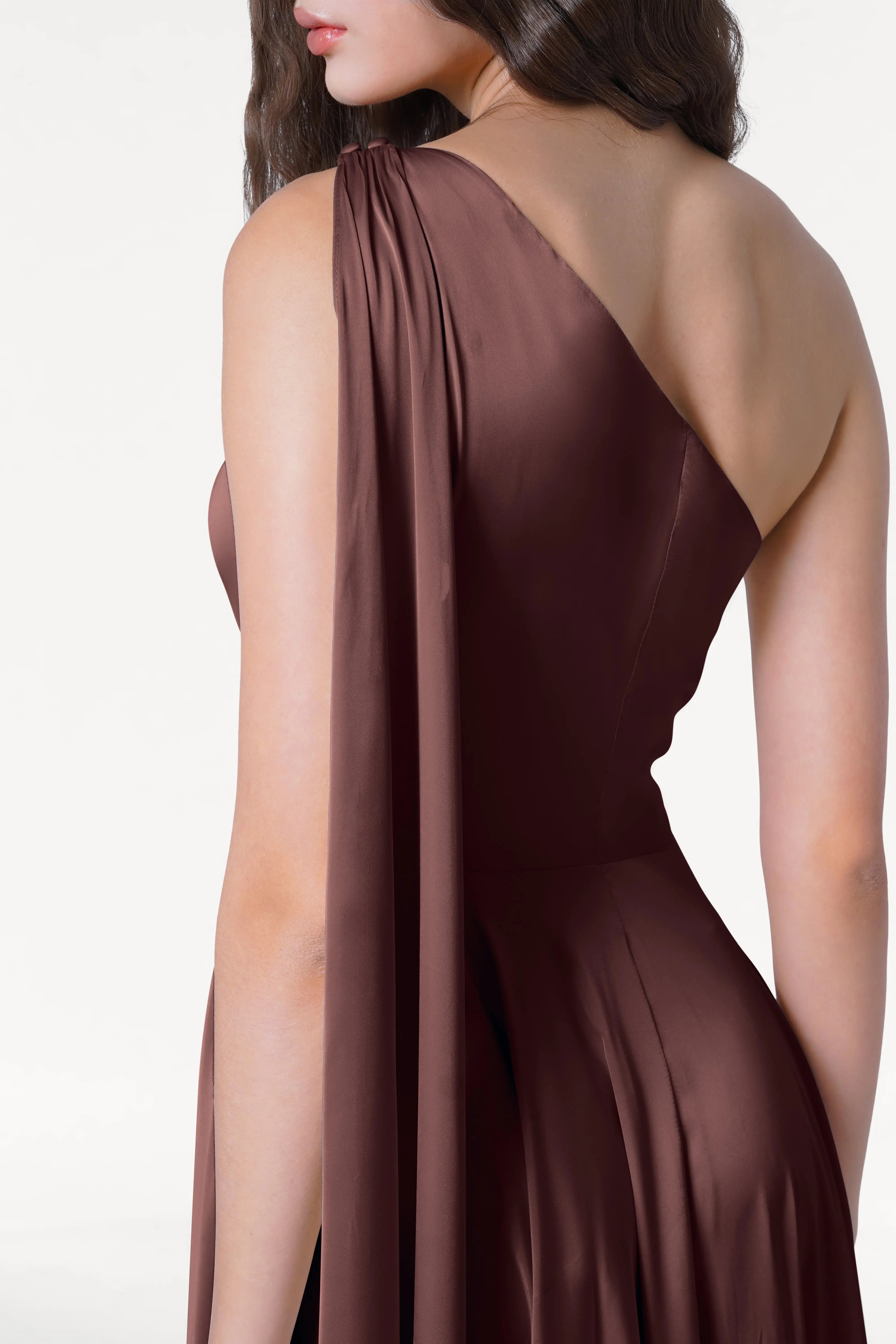 A woman models the TH&TH Lyra Bridesmaid Dress in Chocolate Brown Satin against a white background, her face partially hidden and wavy hair elegantly draped over one shoulder.