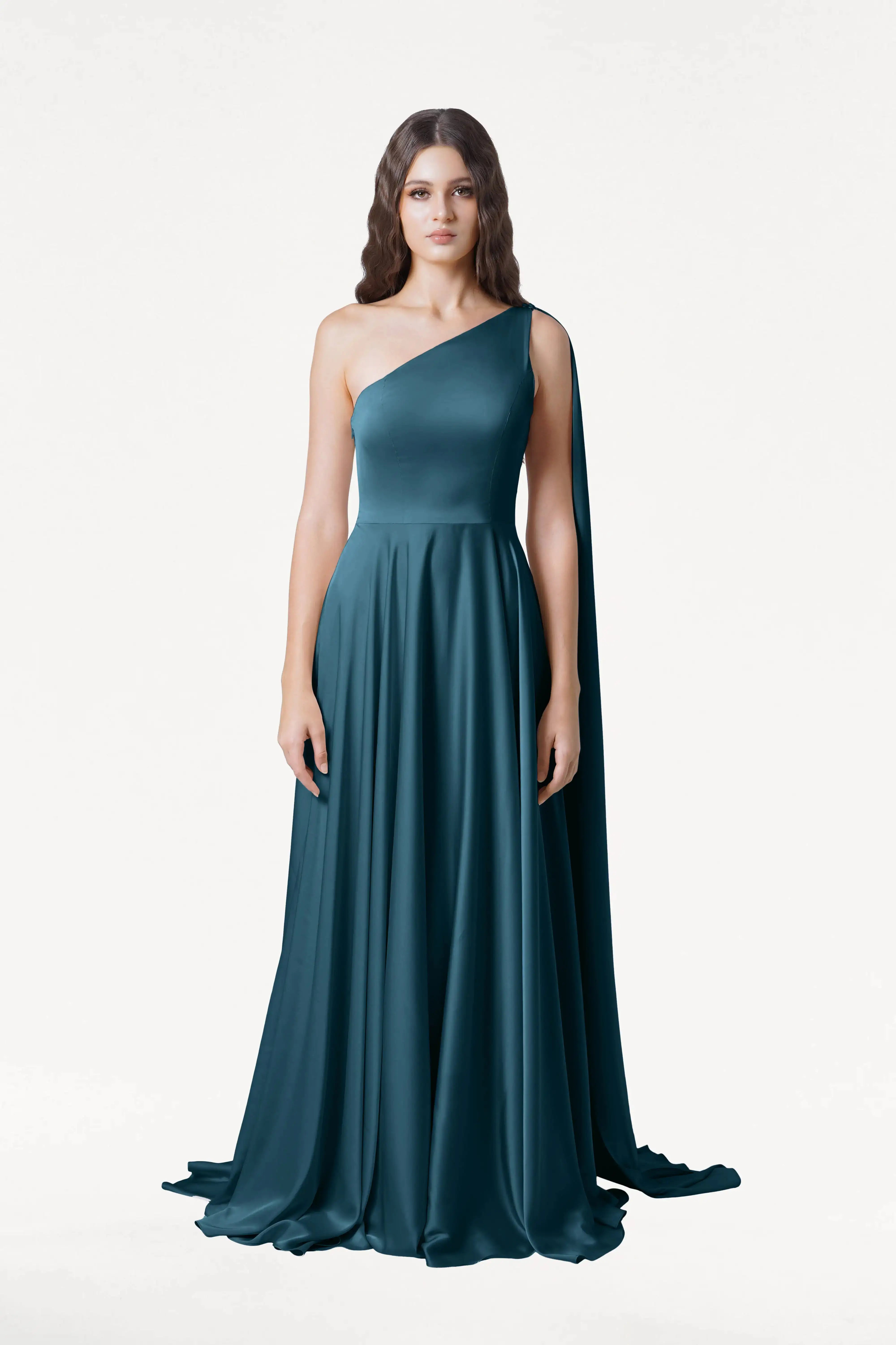 A woman poses in the TH&TH Lyra Bridesmaid Dress in Emerald Dawn Satin—a teal, one-shoulder gown with flowing fabric, a long side drape, and size-inclusive design—against a plain white background.