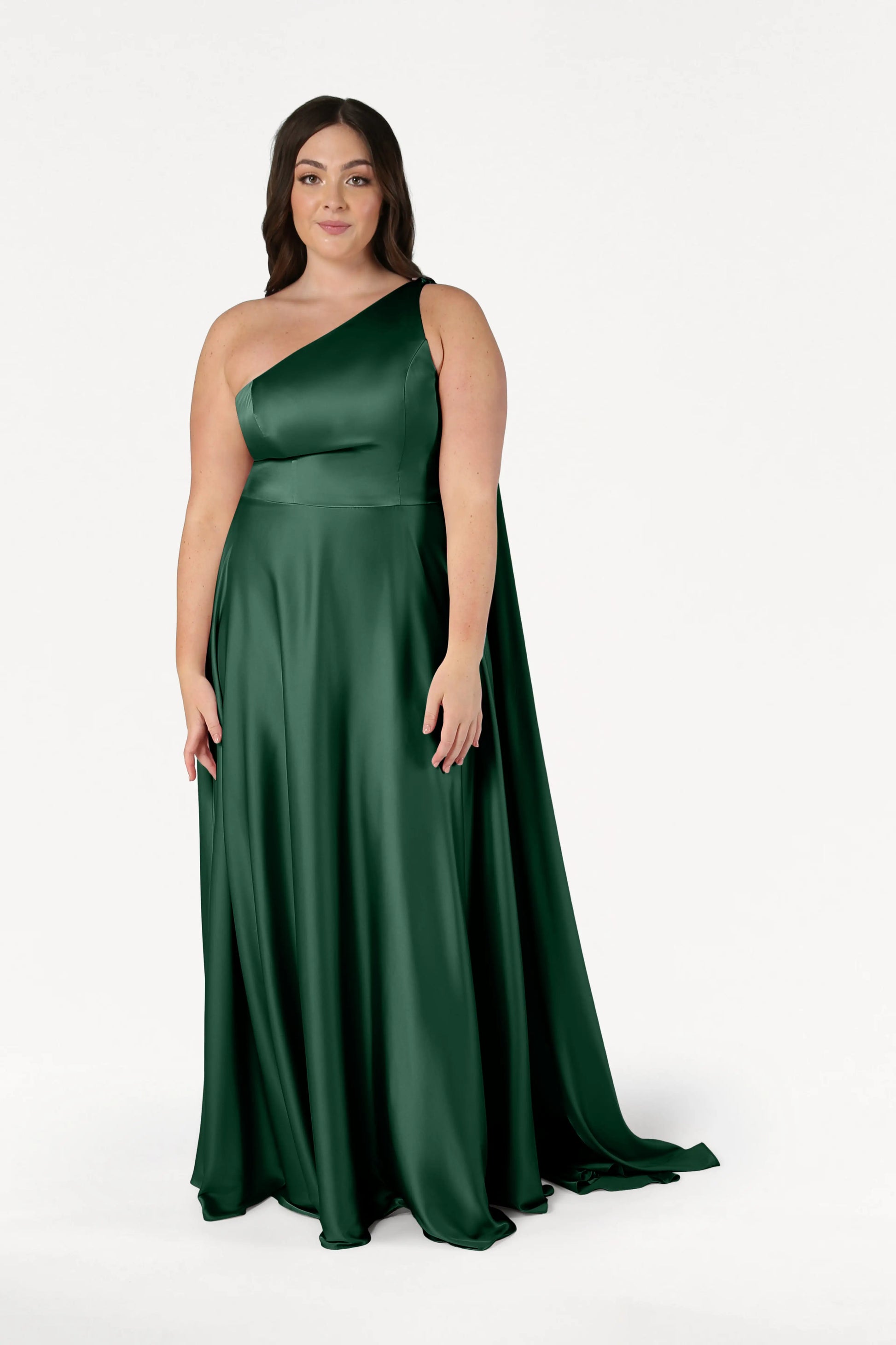 A woman wears the TH&TH Lyra Bridesmaid Dress in Olive Grove Satin, a size-inclusive, floor-length, one-shoulder gown, standing against a plain white background.