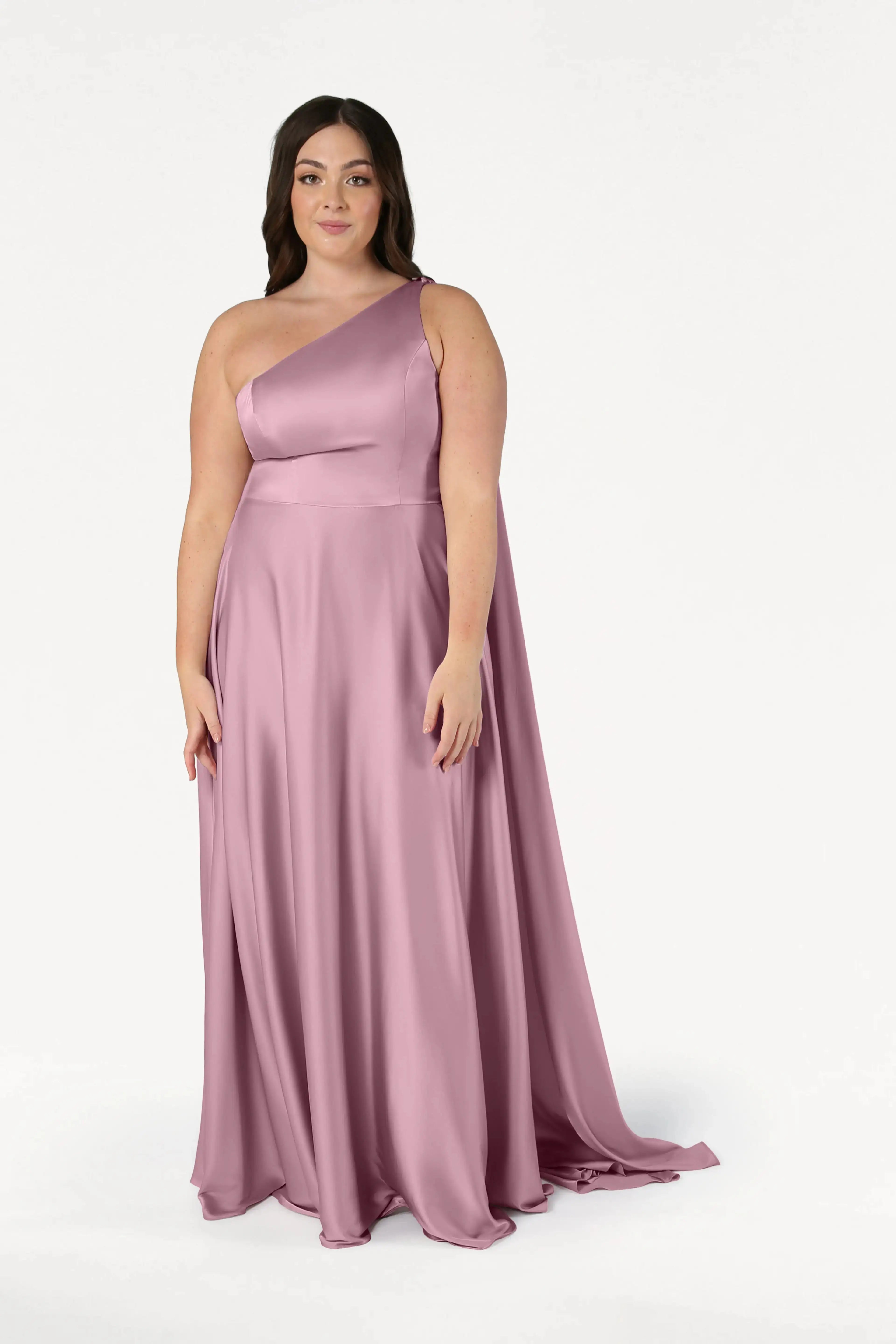 A woman wearing the TH&TH Lyra Bridesmaid Dress in rose pink satin stands against a plain white background, looking forward with a gentle expression.