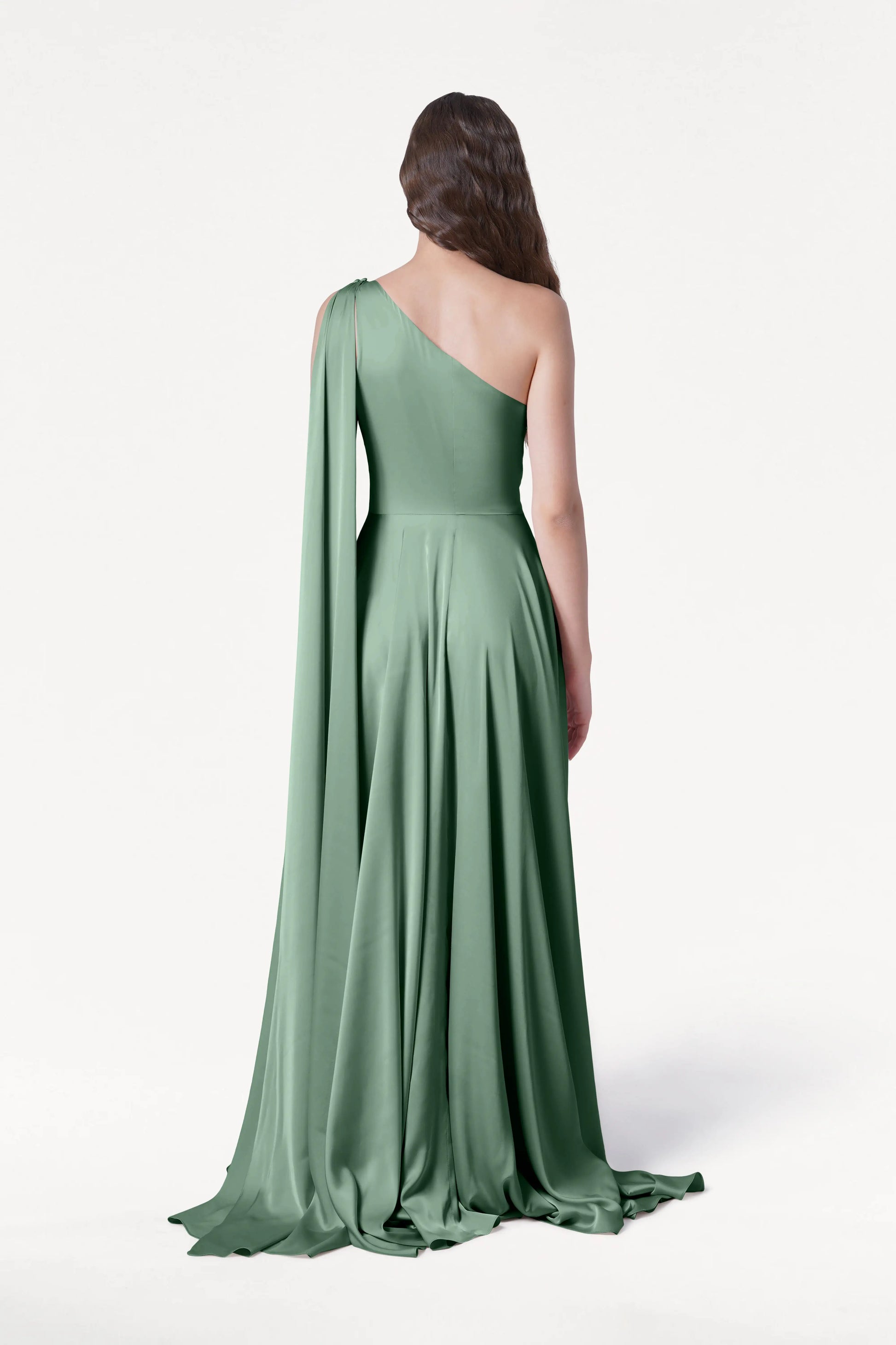 A woman stands facing away against a white background, wearing the TH&TH Lyra Bridesmaid Dress in Sage Green Satin—a size-inclusive, one-shoulder gown with draped sleeve and flowing floor-length skirt.