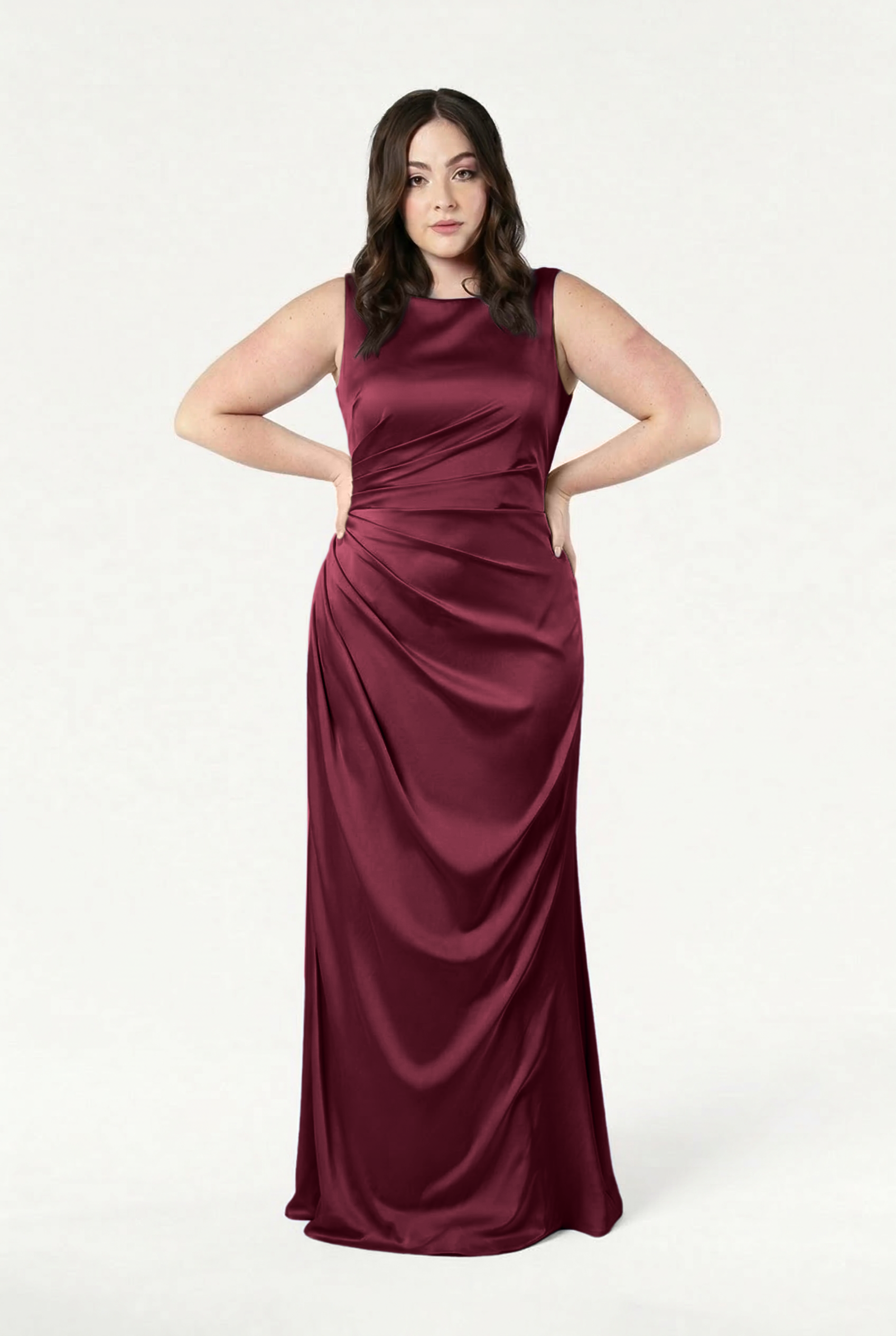 A woman with long dark hair and a neutral expression poses against a white background, wearing the TH&TH Nala Bridesmaid Dress in Merlot Satin—a size-inclusive, floor-length gown with Grecian-inspired pleating.