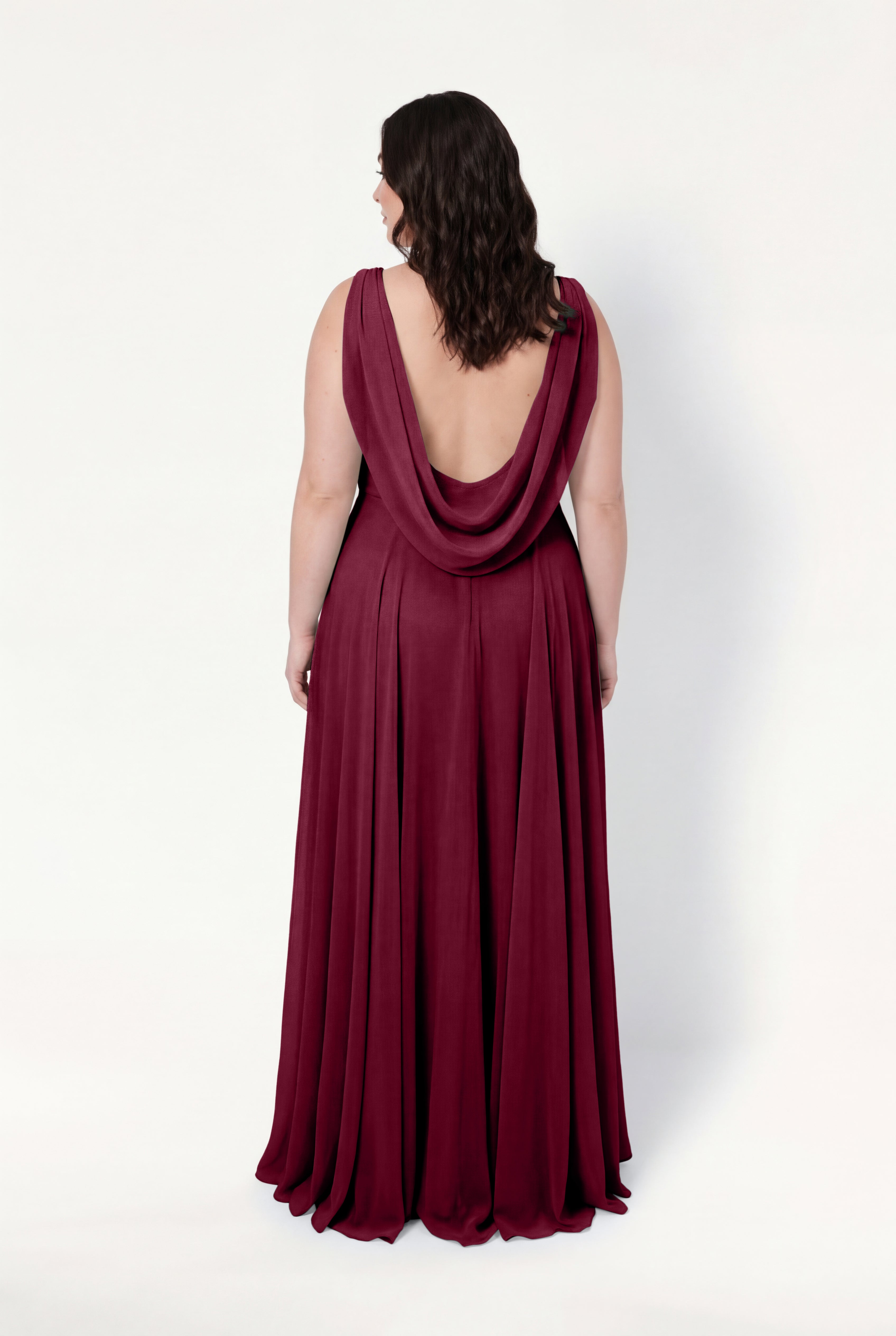 A woman with wavy brown hair faces away, wearing the TH&TH Athena Bridesmaid Dress in Merlot Chiffon—a sleeveless, floor-length gown with a draped open back—set against a plain white background.