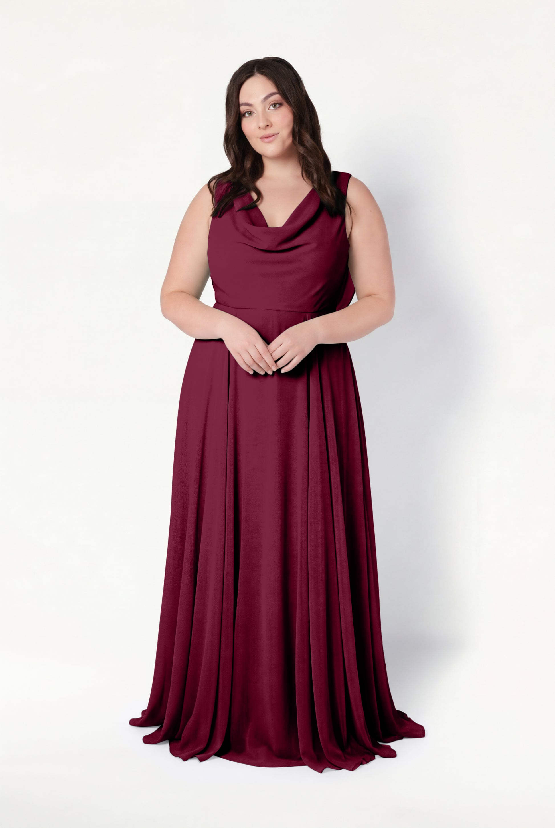 A woman with long brown hair stands against a white background, wearing the TH&TH Athena Bridesmaid Dress in Merlot Chiffon, featuring a sleeveless cowl neck and flowing skirt. She looks ahead, hands gently clasped.
