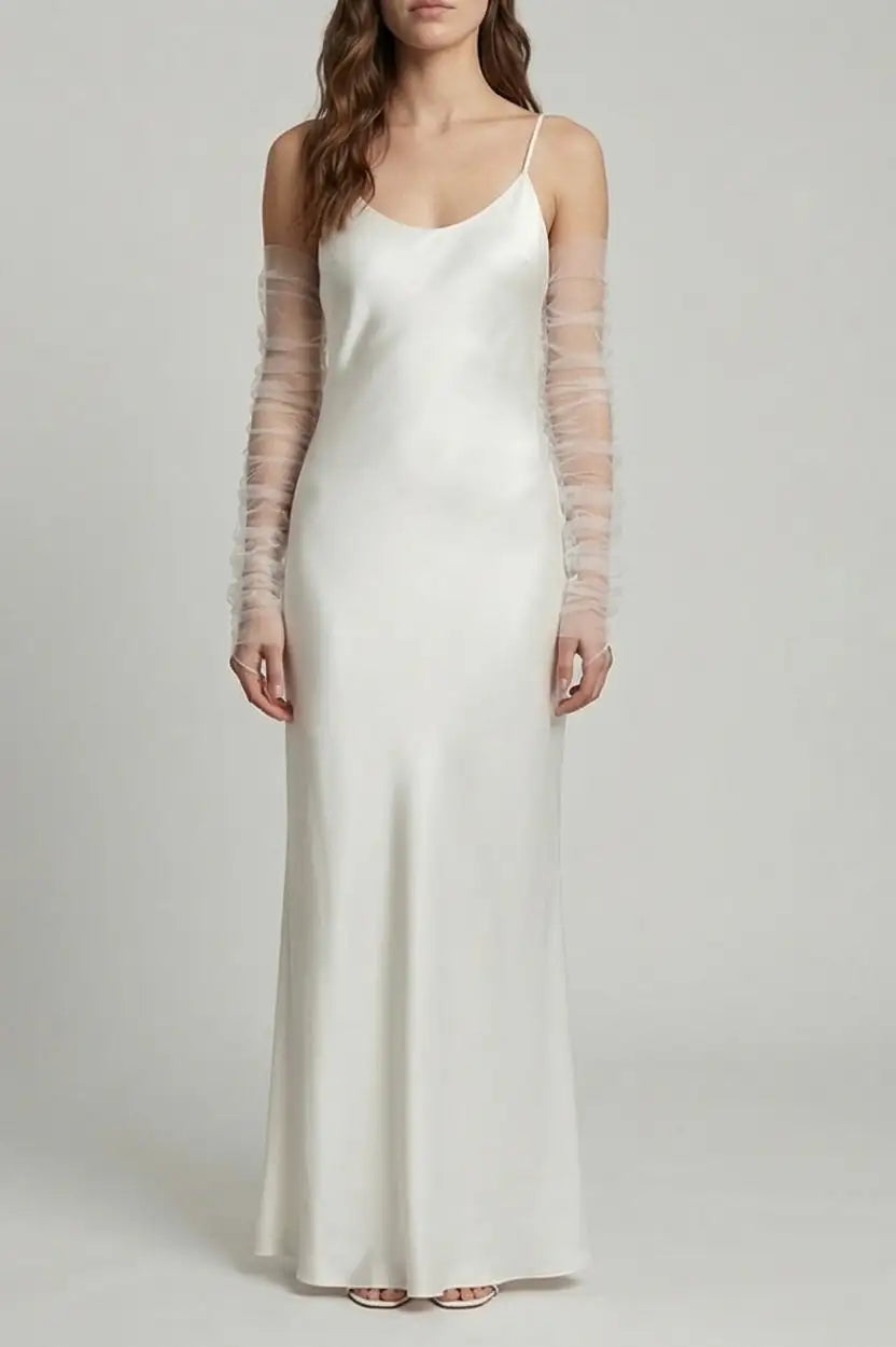 A woman wears the TH&TH Millie Ruched Tulle Opera Sleeves in Ivory with a minimalist, floor-length white satin gown featuring thin spaghetti straps and a slightly flared hem.