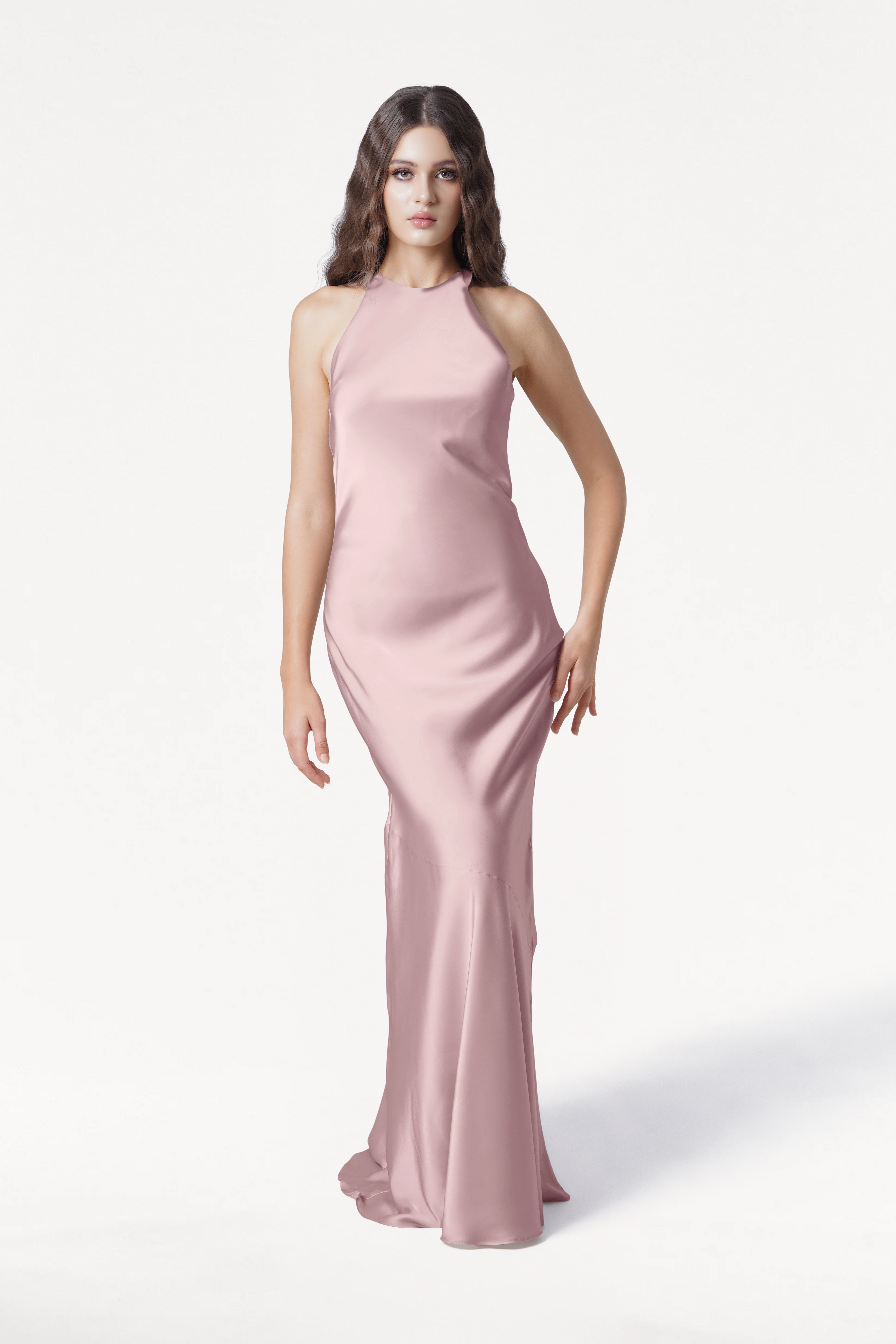 A woman with long wavy brown hair wears the TH&TH Mira Bridesmaid Dress in Smoked Blush Satin—a floor-length, sleeveless gown with a subtle bias-cut—standing against a white background and looking at the camera neutrally.