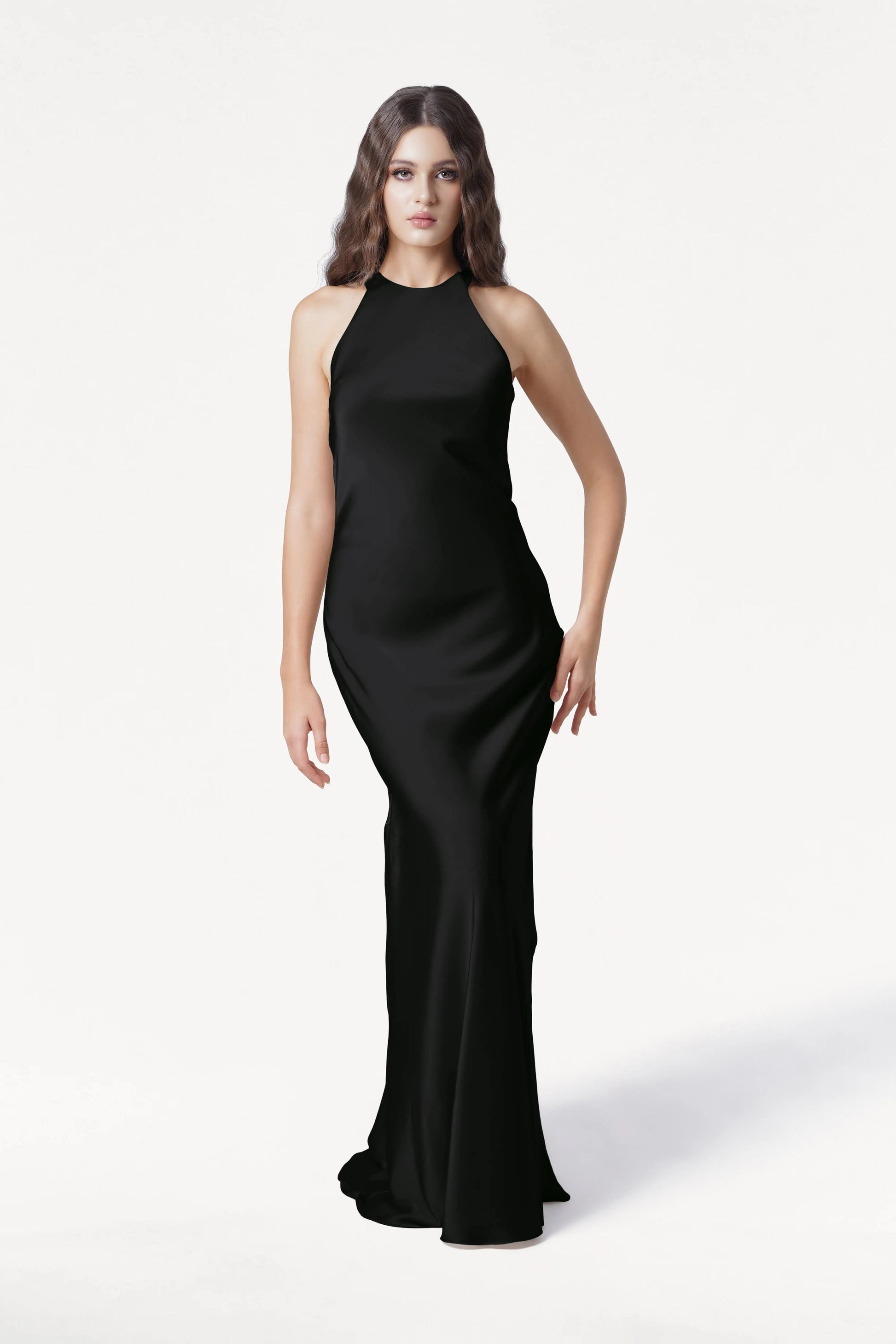 A woman with long, wavy brown hair wears the TH&TH Mira Bridesmaid Dress in black satin, sleeveless and floor-length, standing against a plain white background.