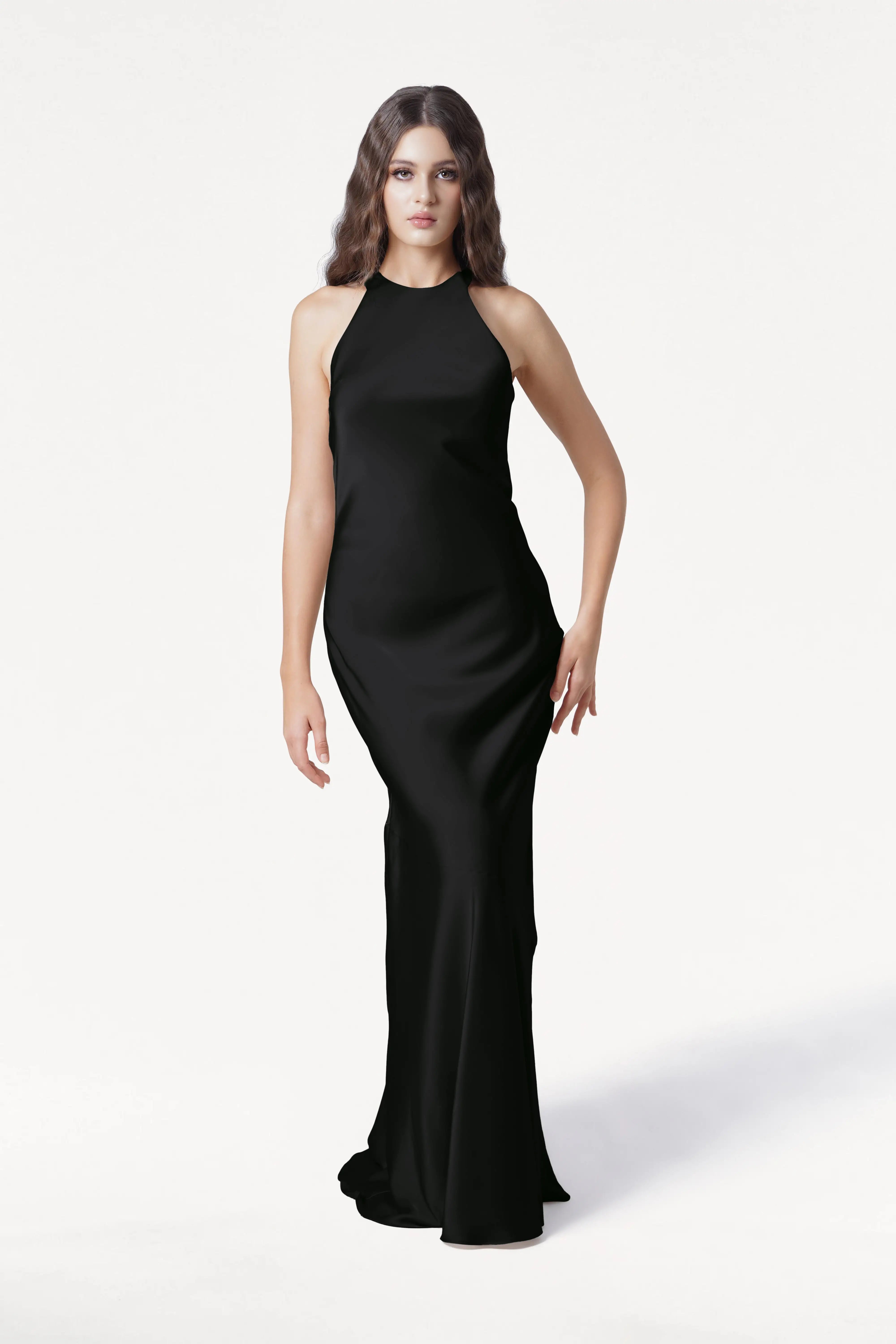 A woman with long, wavy brown hair wears the TH&TH Mira Bridesmaid Dress in black satin, sleeveless and floor-length, standing against a plain white background.