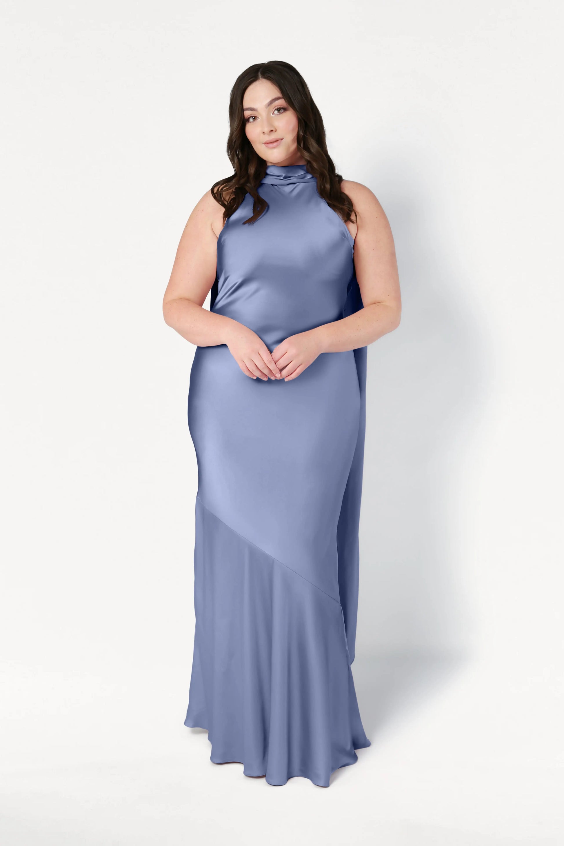 A woman with long dark hair models the TH&TH Mira Bridesmaid Dress in French Blue Satin, a sleeveless, high-neck, floor-length gown that drapes elegantly as she stands against a plain white background.