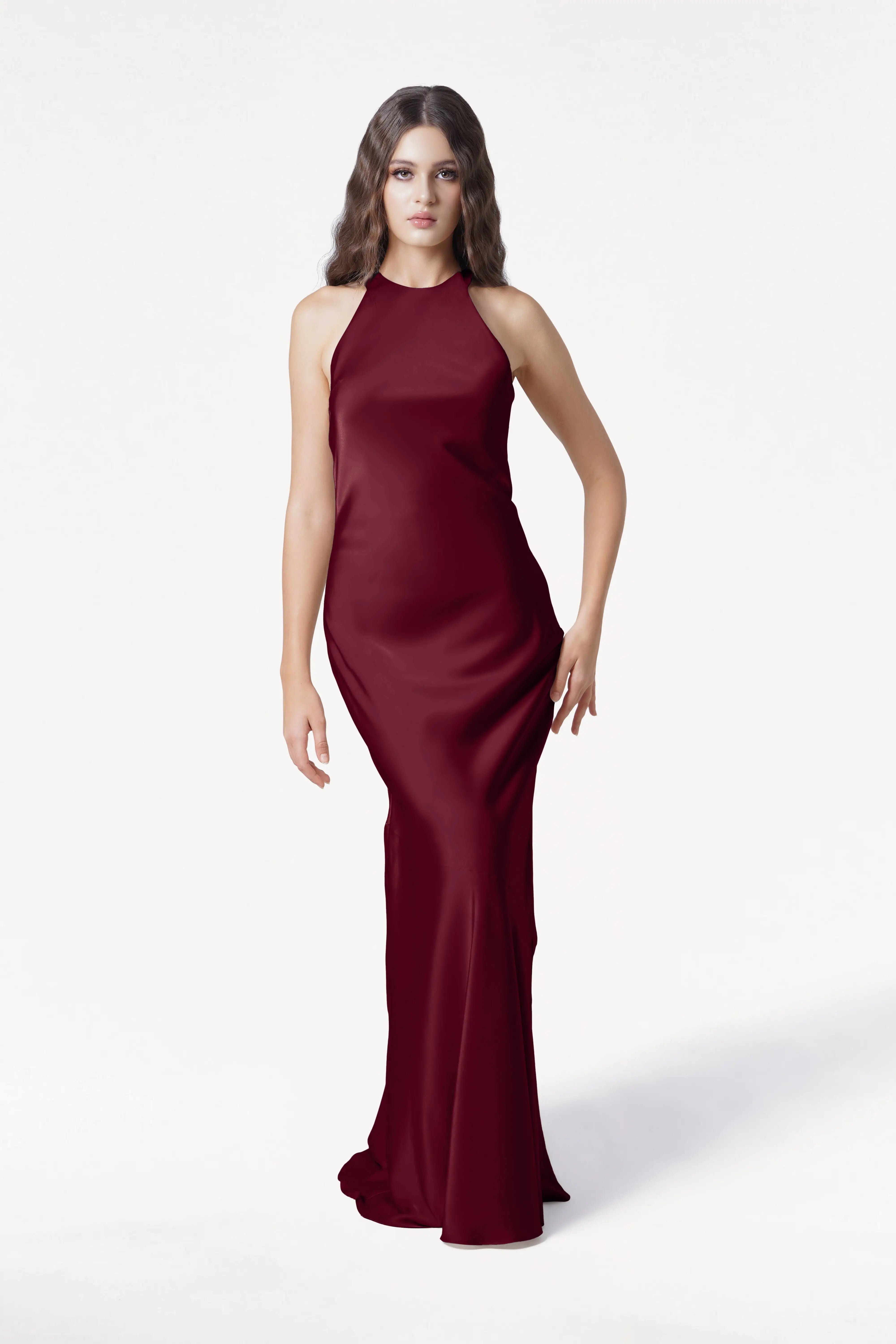 A woman with long wavy brown hair wears the TH&TH Mira Bridesmaid Dress in Merlot Satin. The sleeveless, floor-length gown is shown against a plain white background as she looks forward with a neutral expression.