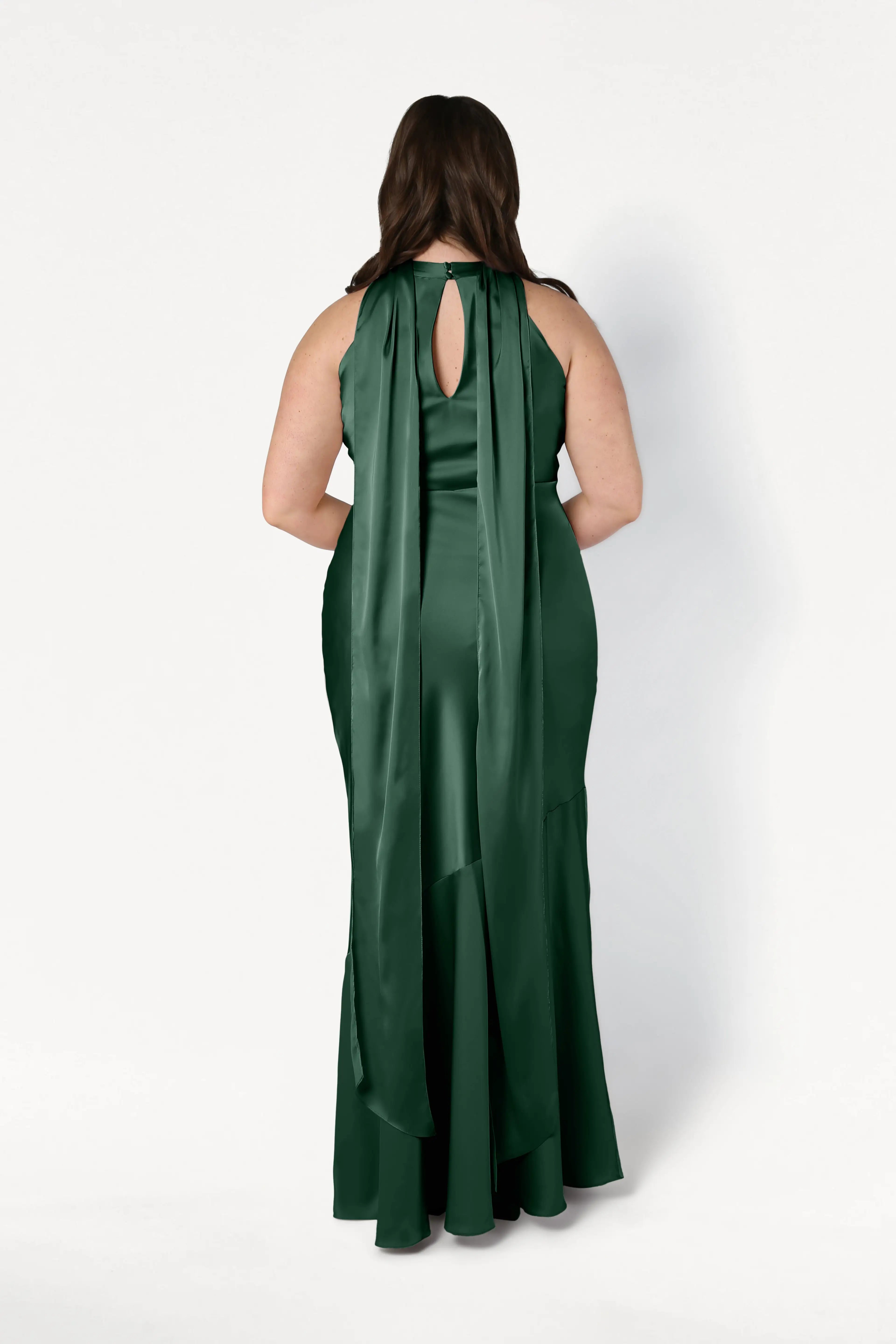 Back view of a model in the Mira Bridesmaid Dress by TH&TH, crafted from Olive Grove satin with a halter neck, keyhole back, flowing cape detail, and fishtail hem.