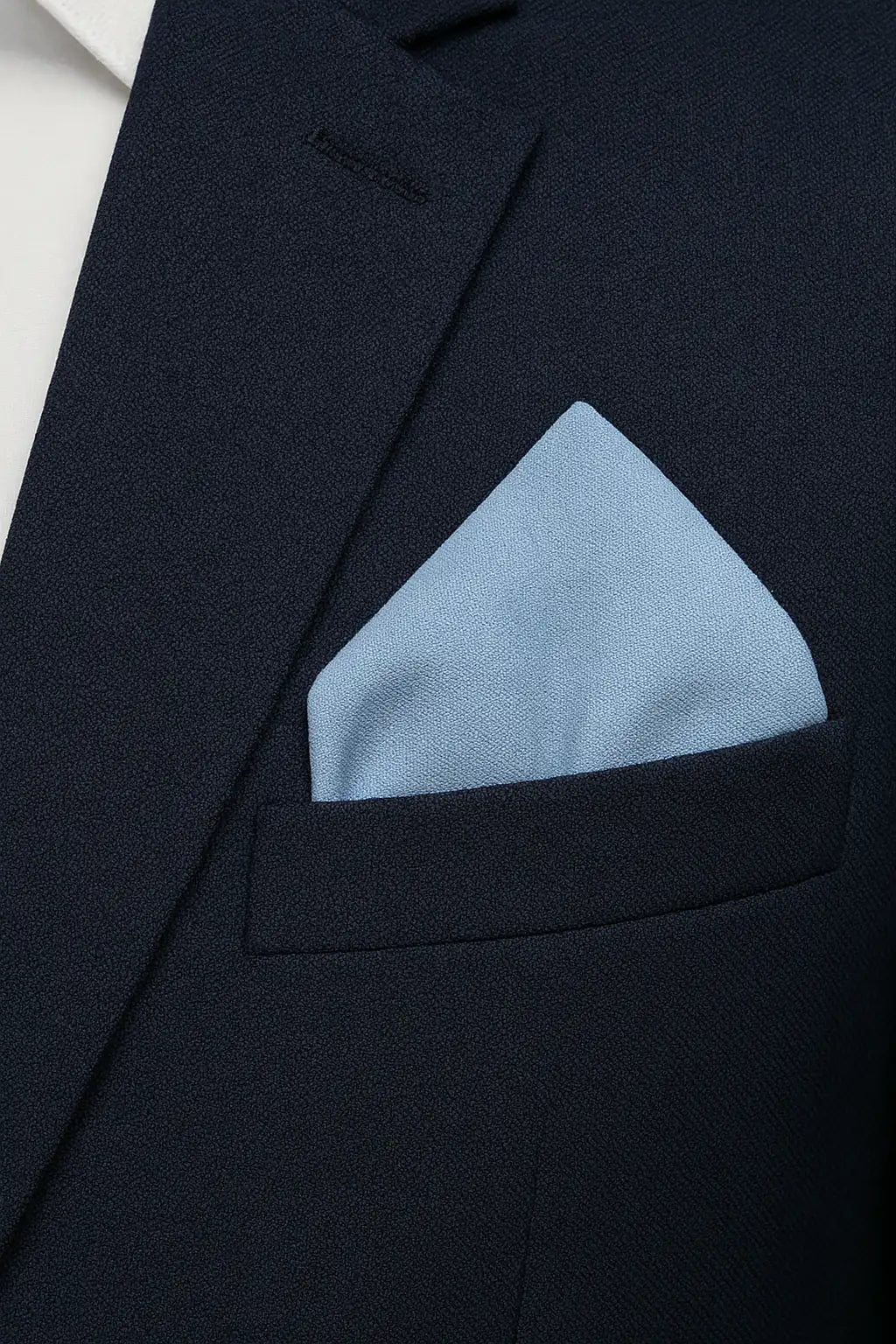 A close-up of a dark navy suit jacket featuring the TH&TH Moss Crepe Pocket Square in light blue, neatly folded in the breast pocket over a white shirt—an ideal wedding or formal occasion accessory.