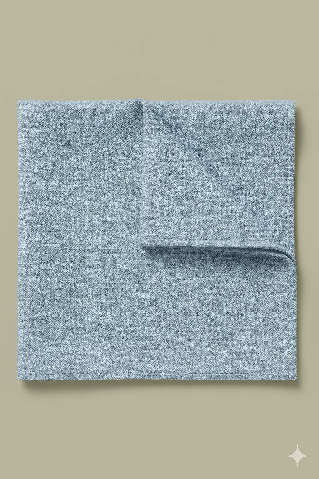 A neatly folded light blue TH&TH Moss Crepe Pocket Square with a flipped-up corner, displayed on a plain beige surface—an elegant accessory ideal for complementing bridesmaid dresses at weddings.
