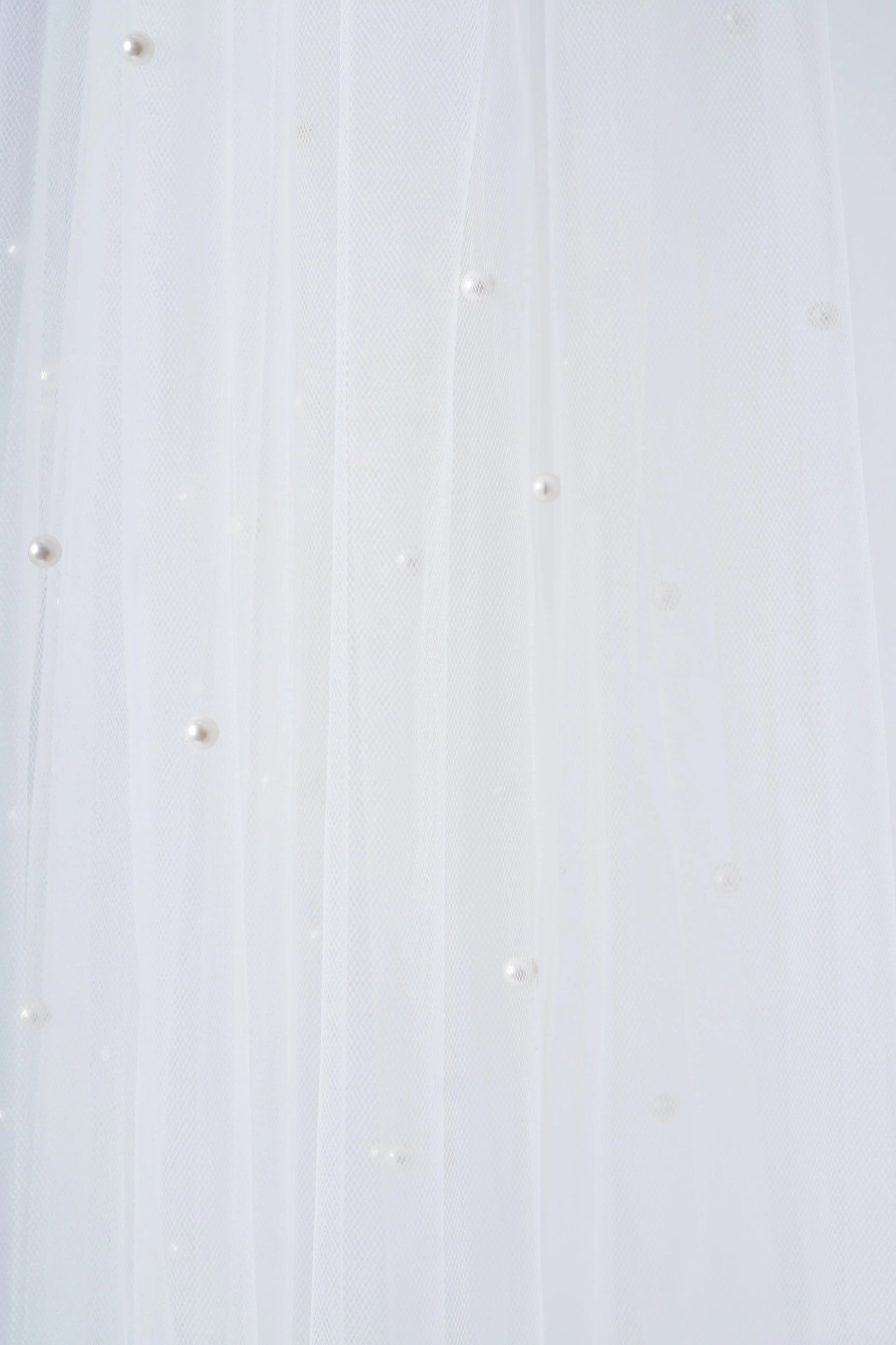 The Muse Pearl Scatter Veil by TH&TH features sheer white tulle adorned with delicate, scattered pearls, creating a soft and elegant texture—perfect for bridal wear.