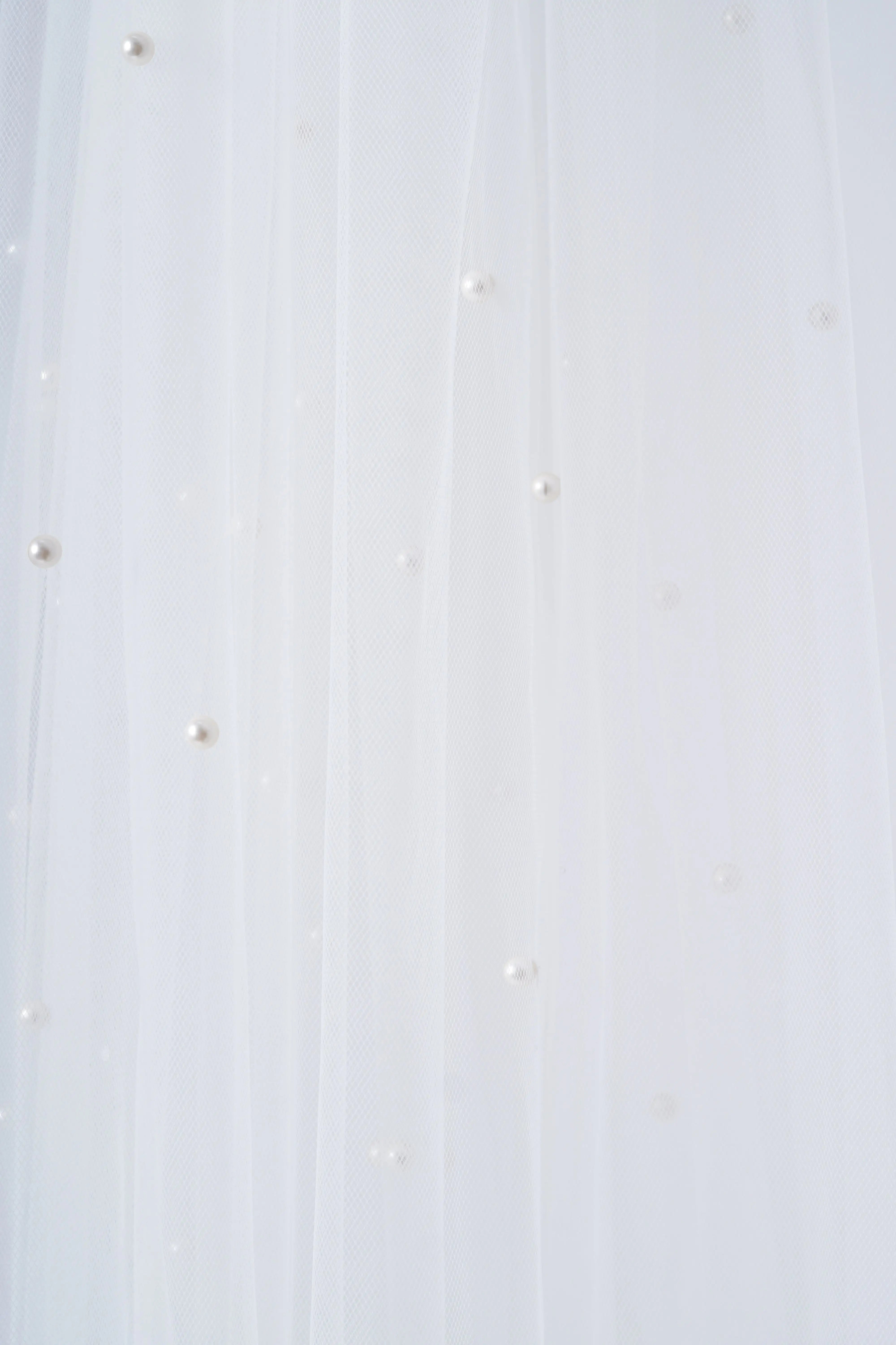 The Muse Pearl Scatter Veil by TH&TH features sheer white tulle adorned with delicate, scattered pearls, creating a soft and elegant texture—perfect for bridal wear.