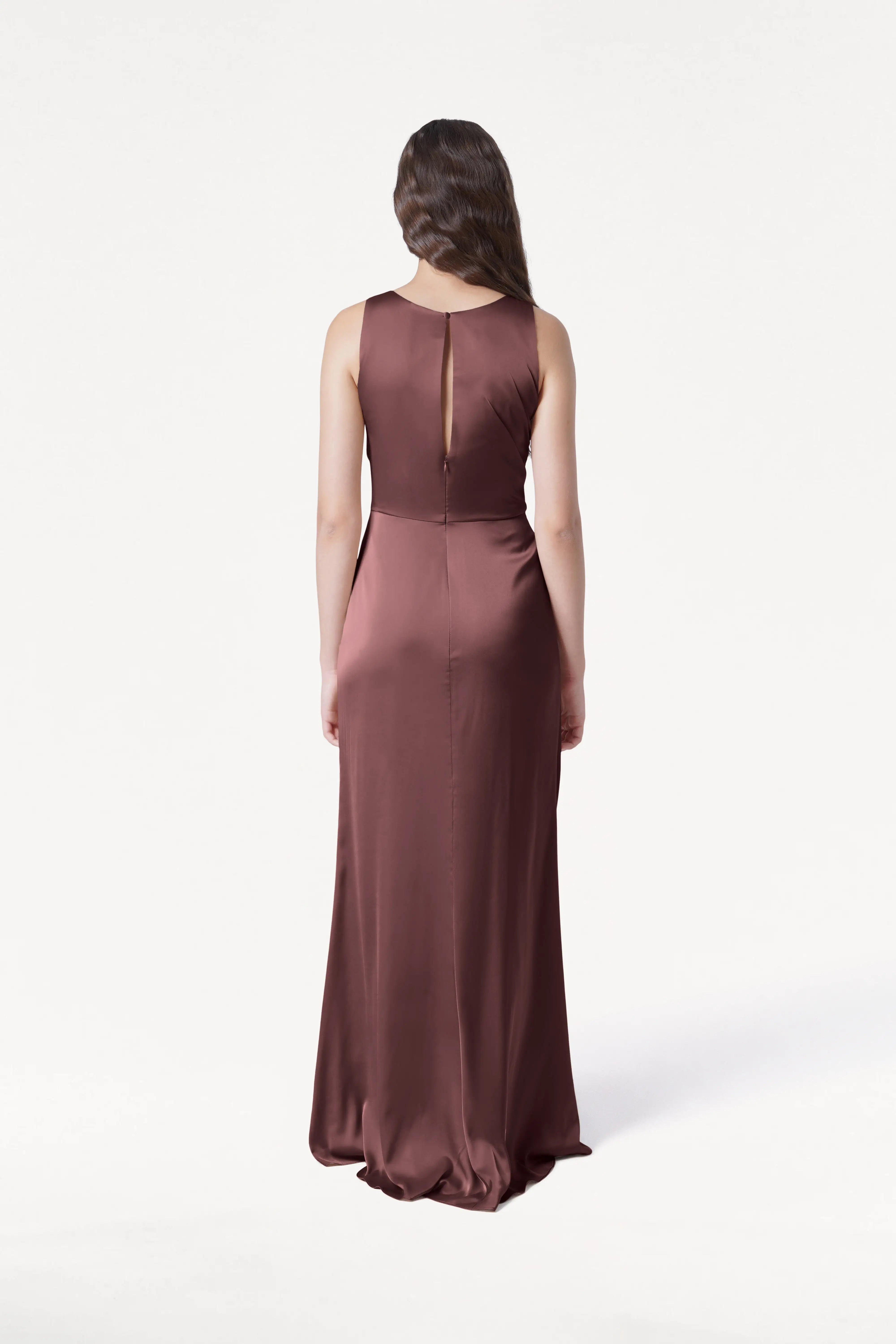 A woman with long brown hair faces away, wearing the TH&TH Nala Bridesmaid Dress in chocolate brown satin, featuring Grecian pleating and a keyhole back—an elegant choice for modern weddings against a plain white background.