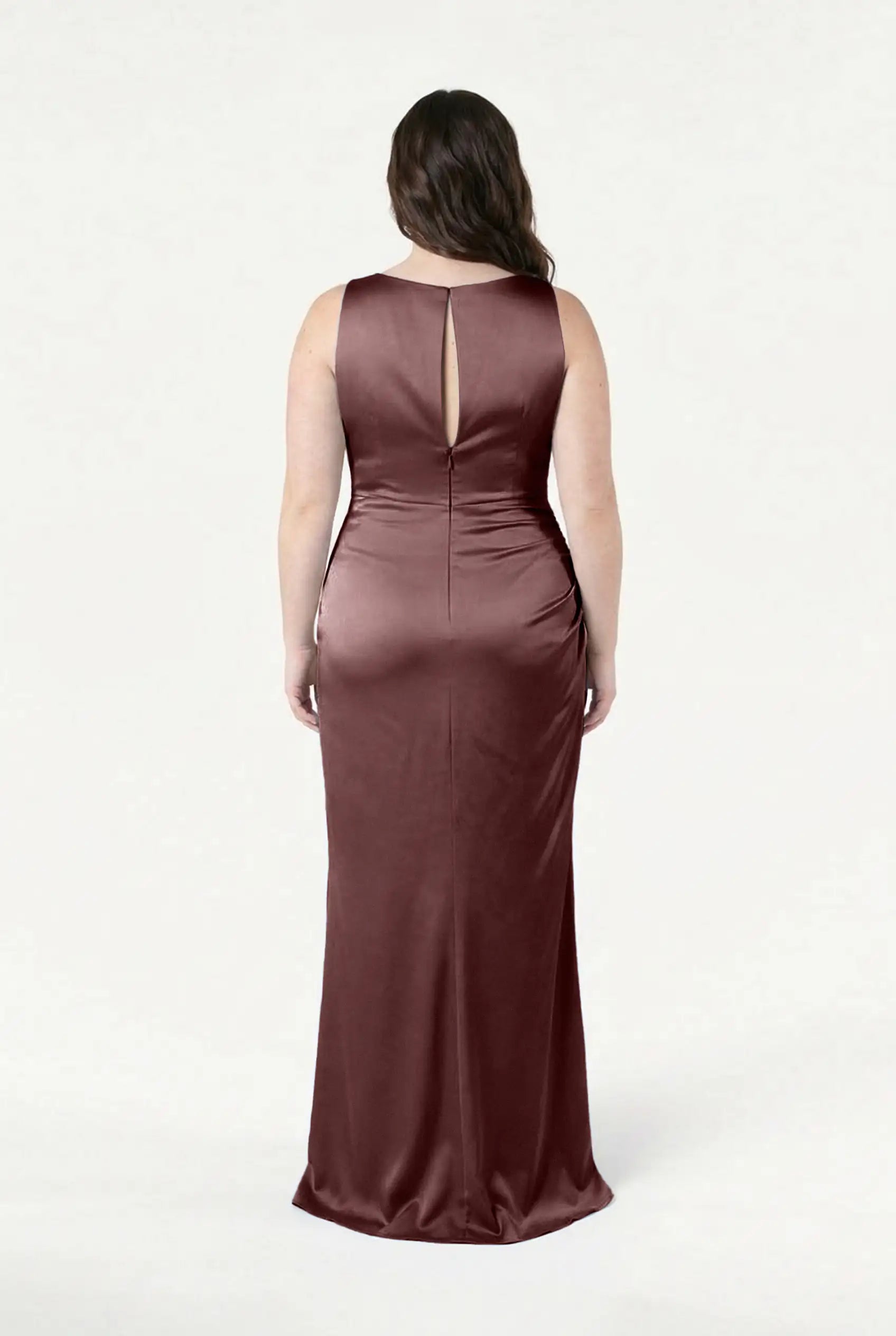 A woman faces away, wearing the Nala Bridesmaid Dress in Chocolate Brown Satin by TH&TH. This long, sleeveless dress features Grecian pleating and a back keyhole, ideal for modern weddings, set against a plain white background.