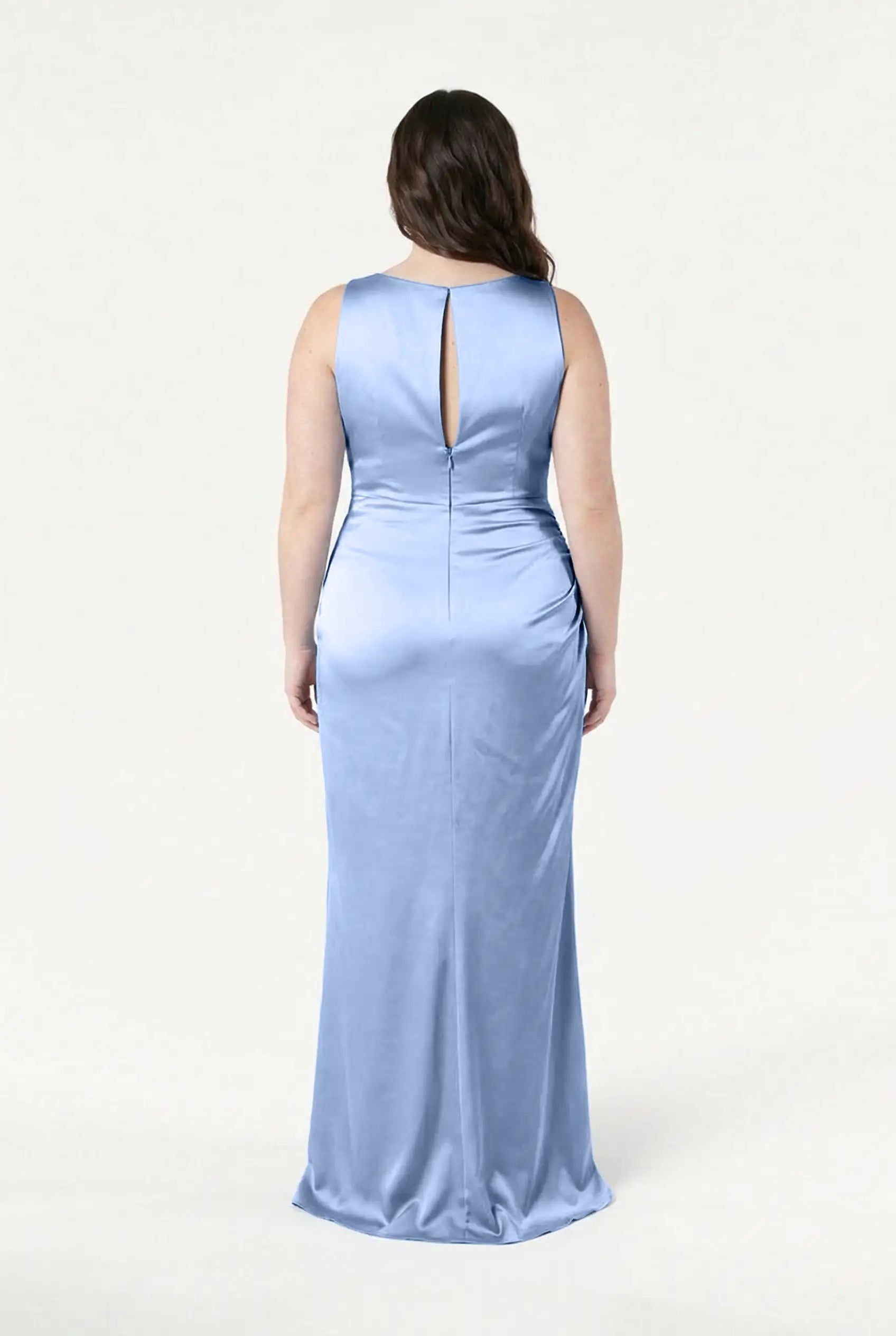 A woman faces away, wearing the TH&TH Nala Bridesmaid Dress in Dusty Blue Satin. This size-inclusive, floor-length gown features a keyhole back and subtle side ruching, set against a plain white background.