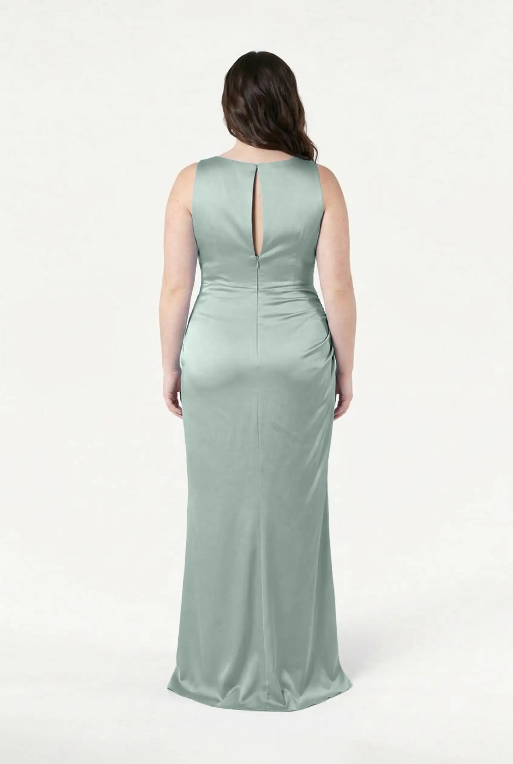 A woman faces away, wearing the TH&TH Nala Bridesmaid Dress in Dusty Eucalyptus Satin—a sleeveless, floor-length gown with a keyhole back, subtle Grecian pleating, and smooth shiny fabric. The background is plain white.