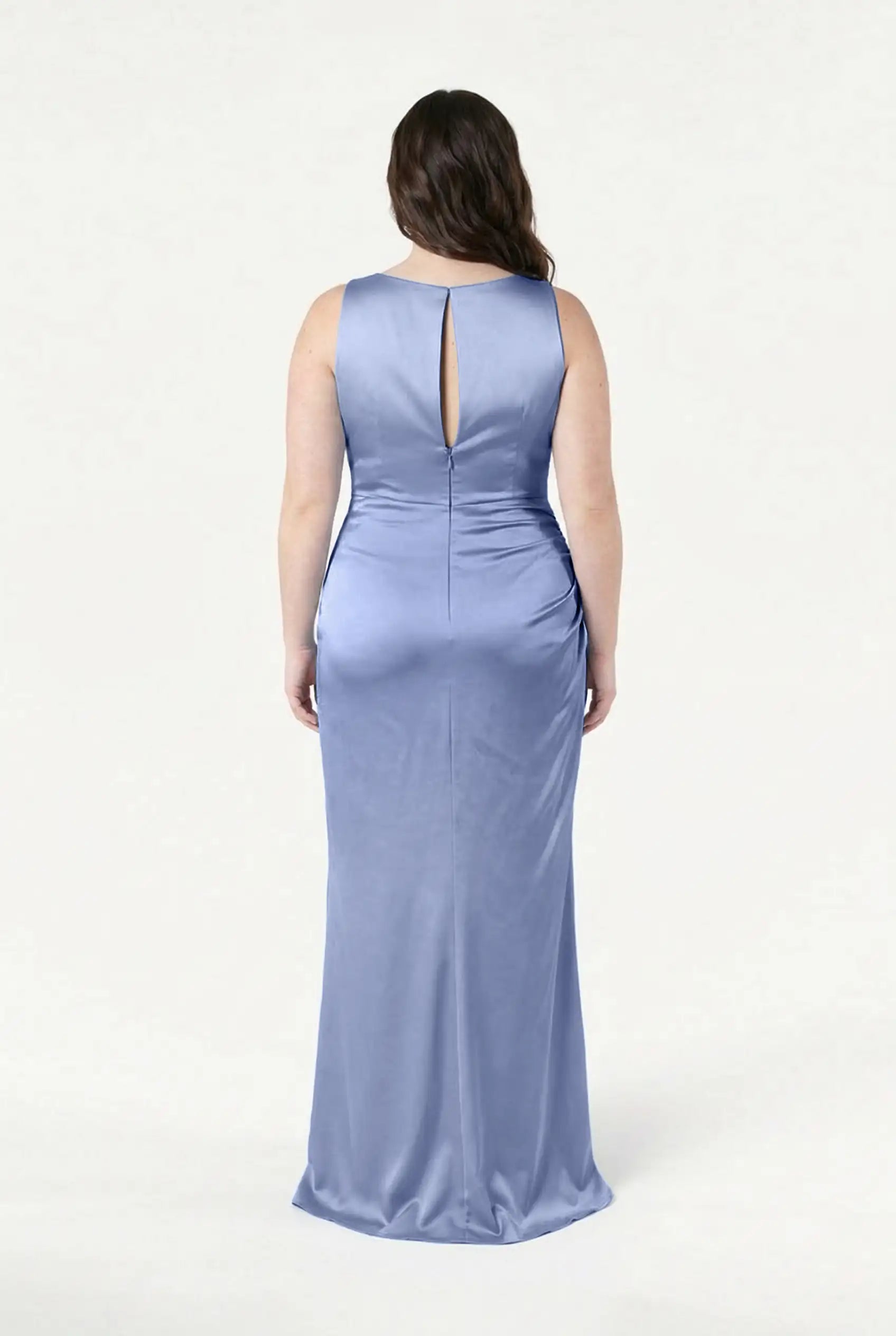 A woman faces away, wearing the TH&TH Nala Bridesmaid Dress in French Blue Satin—a size-inclusive, fitted, floor-length gown with a keyhole back and smooth sheen—against a plain white background.