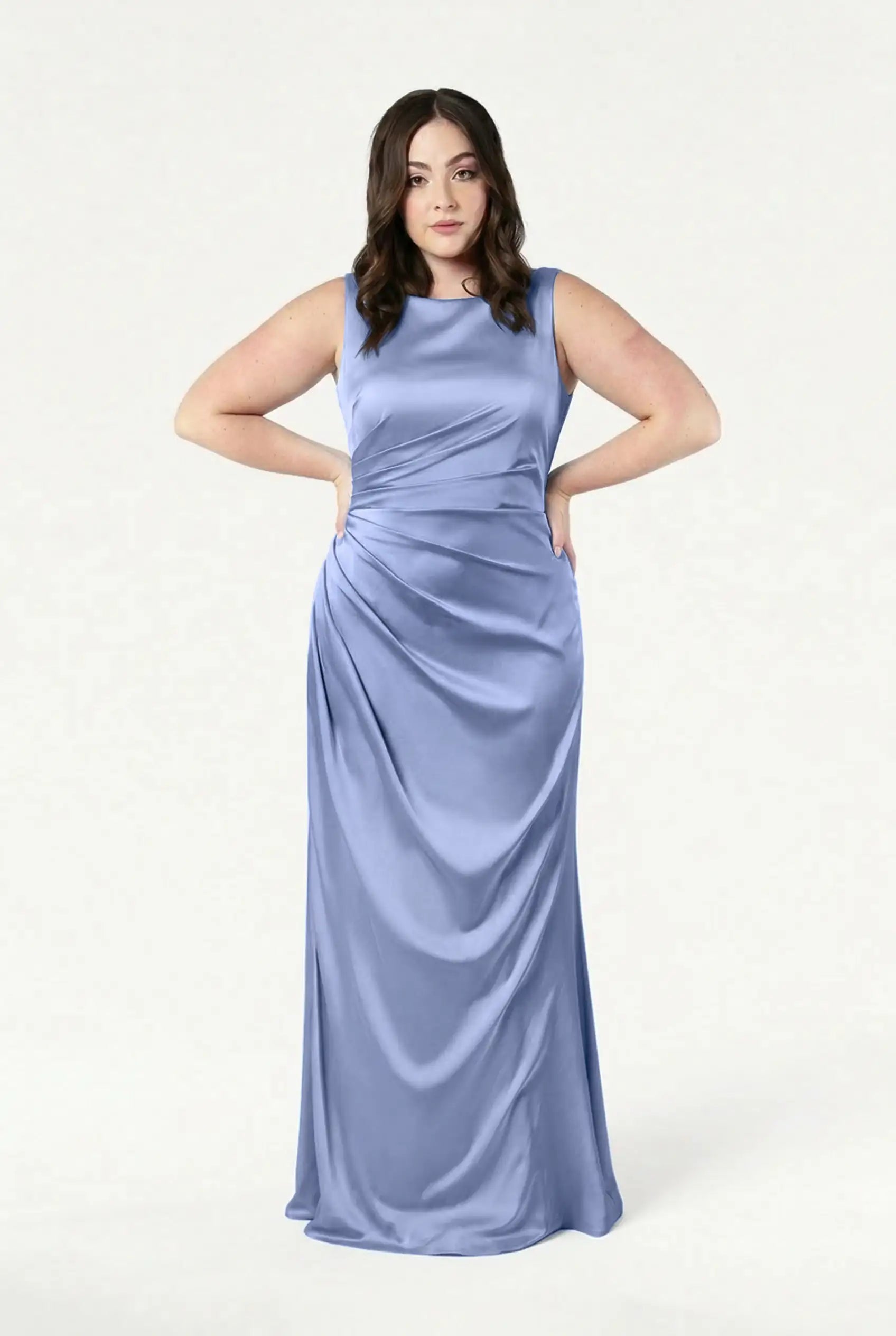 A woman with medium-length brown hair and a calm expression wears the TH&TH Nala Bridesmaid Dress in French Blue Satin, a sleeveless, floor-length gown featuring Grecian-inspired pleating and gathered waist detail against a plain white background.