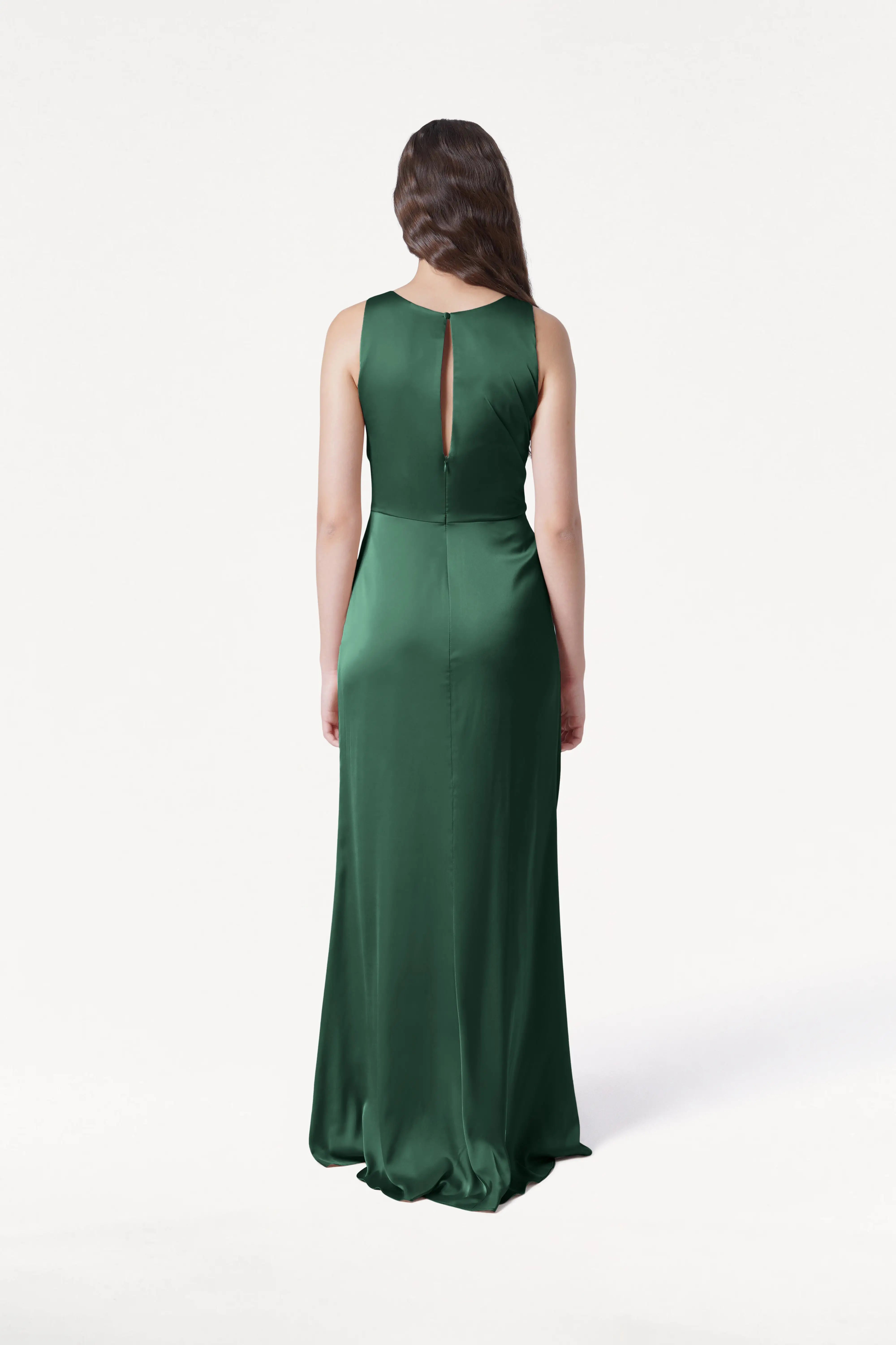 A woman with long brown hair faces away, wearing the TH&TH Nala Bridesmaid Dress in Olive Grove Satin—a sleeveless, floor-length gown with a keyhole back—perfect for modern bridal parties, set against a plain white background.