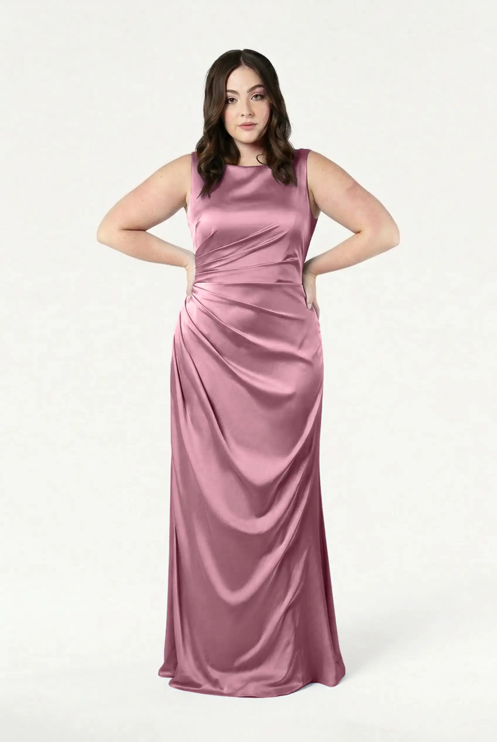 A woman stands confidently in the TH&TH Nala Bridesmaid Dress in rose pink satin, featuring a long, sleeveless design with gathered waist detailing—a chic choice for modern bridal parties—set against a plain white background.