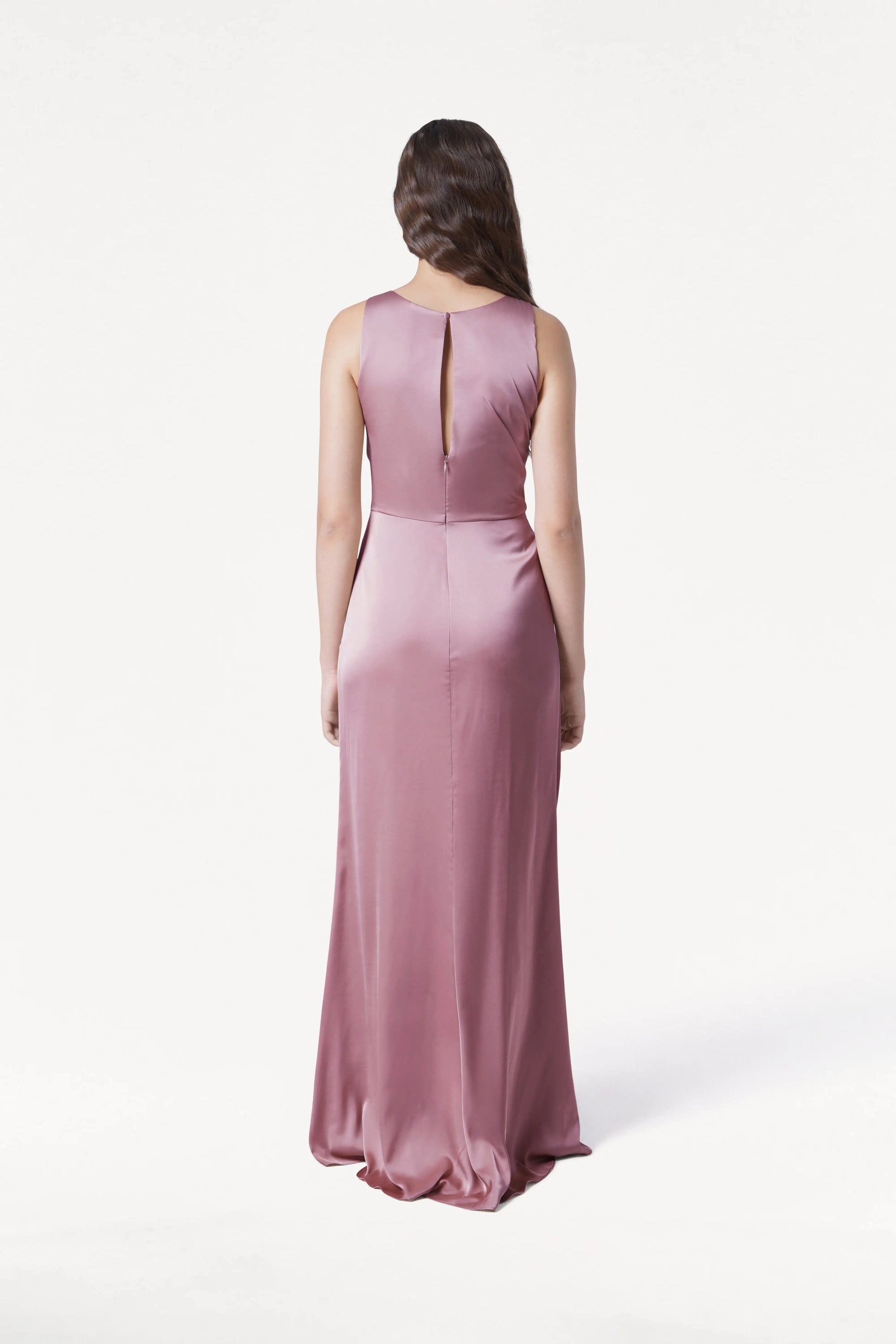 A woman faces away from the camera in the TH&TH Nala Bridesmaid Dress, a floor-length, sleeveless rose pink satin gown featuring a small keyhole back. The background is plain white—perfect for modern bridal parties.