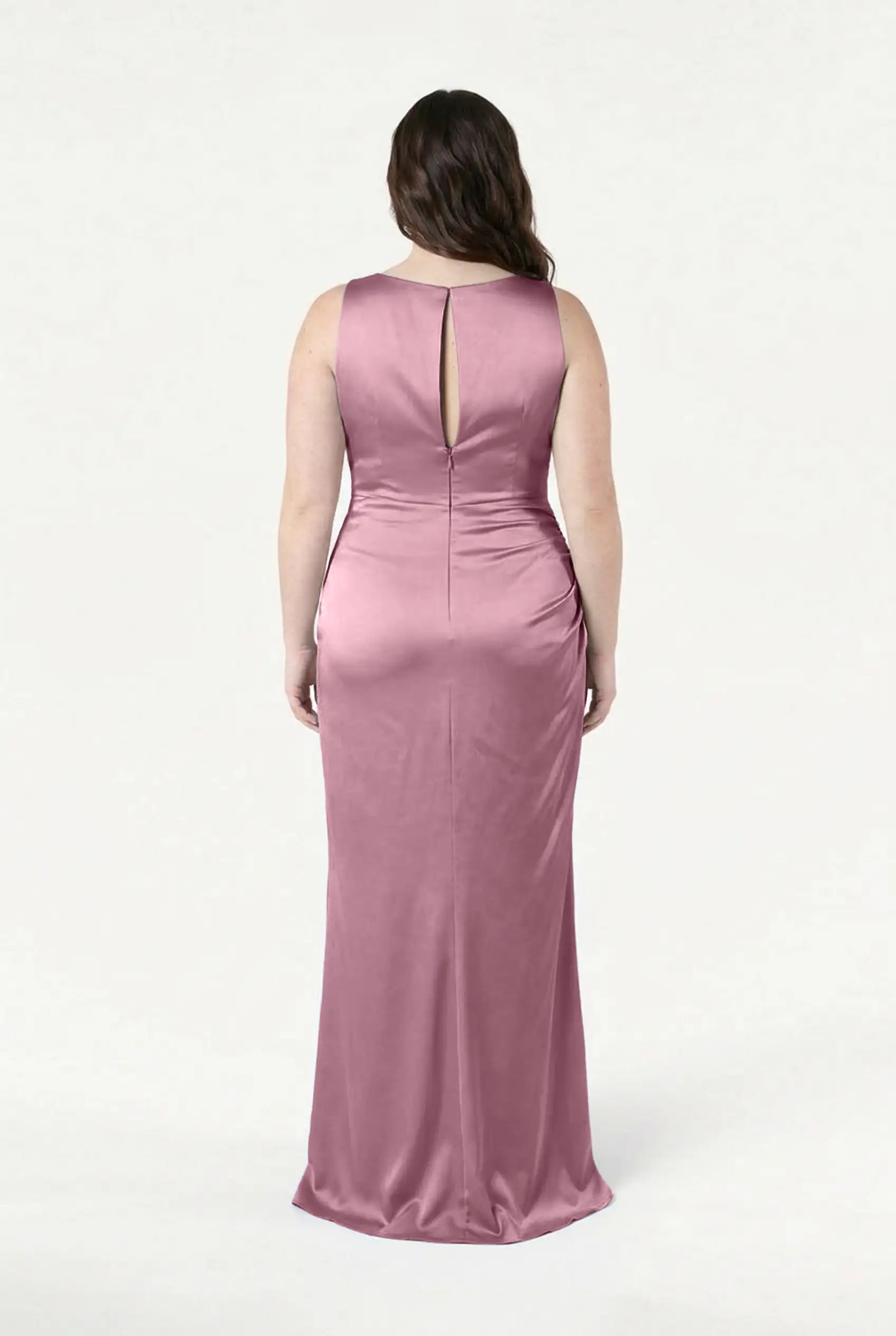 A woman with wavy brown hair is shown from the back, wearing the TH&TH Nala Bridesmaid Dress in rose pink satin, featuring a sleeveless, floor-length design and keyhole back, ideal for modern bridal parties, set against a plain white backdrop.