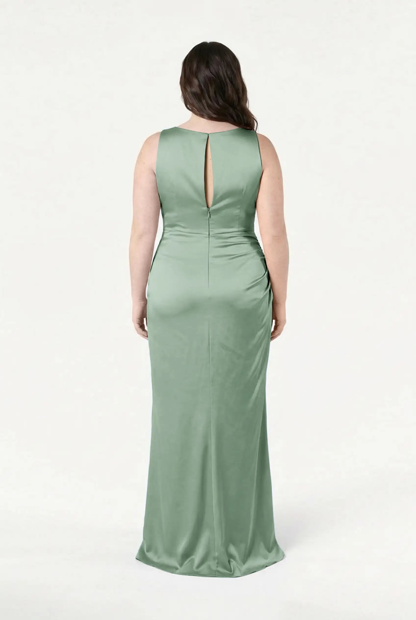 A woman faces away wearing the TH&TH Nala Bridesmaid Dress in Sage Green Satin, a size-inclusive, floor-length gown with Grecian pleating, a keyhole back, and smooth shiny fabric. The background is plain white.