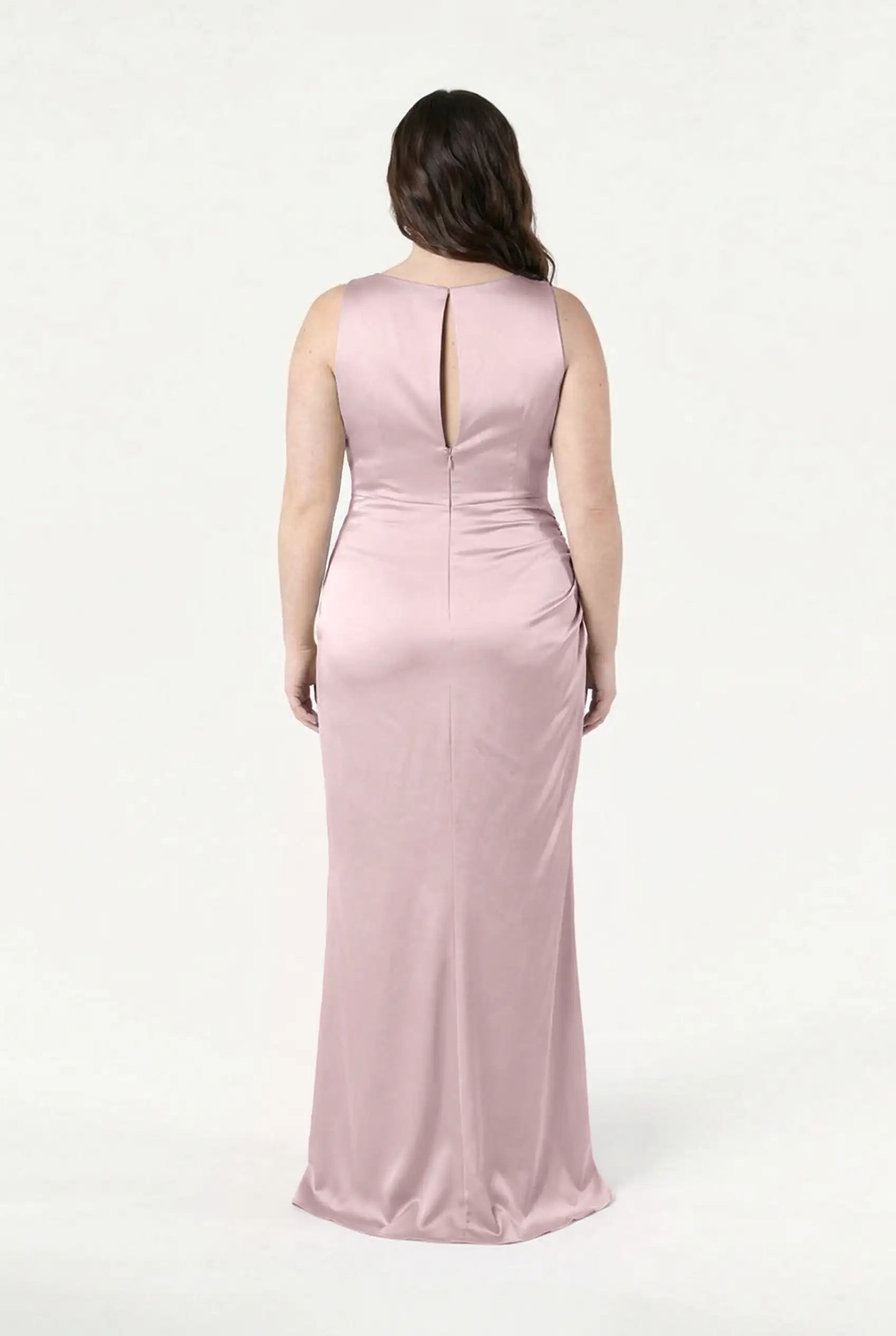 A woman stands with her back to the camera in the TH&TH Nala Bridesmaid Dress in Smoked Blush Satin—a sleeveless, floor-length gown with Grecian-inspired pleating and a small upper-back keyhole, set against a plain white background.