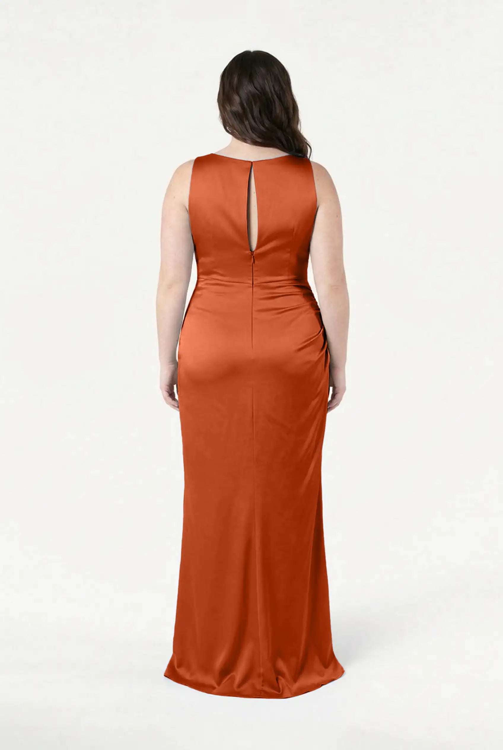 A woman with long dark hair faces away, wearing the TH&TH Nala Bridesmaid Dress in Terracotta Satin. This sleeveless, floor-length gown features a keyhole back and is perfect for modern bridal parties, standing out against a white background.