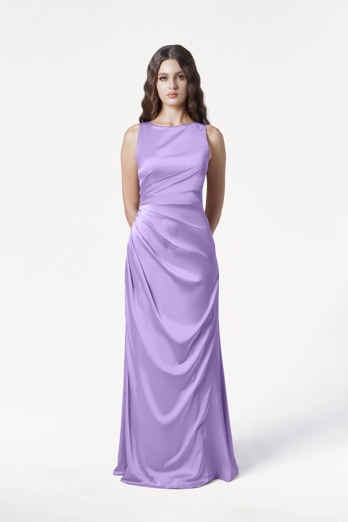 A woman with long wavy brown hair stands against a plain white background, wearing the TH&TH Nala Bridesmaid Dress in Violet Satin, featuring Grecian-inspired pleating and draping. Her hands are held behind her back—a modern, elegant look for bridal parties.
