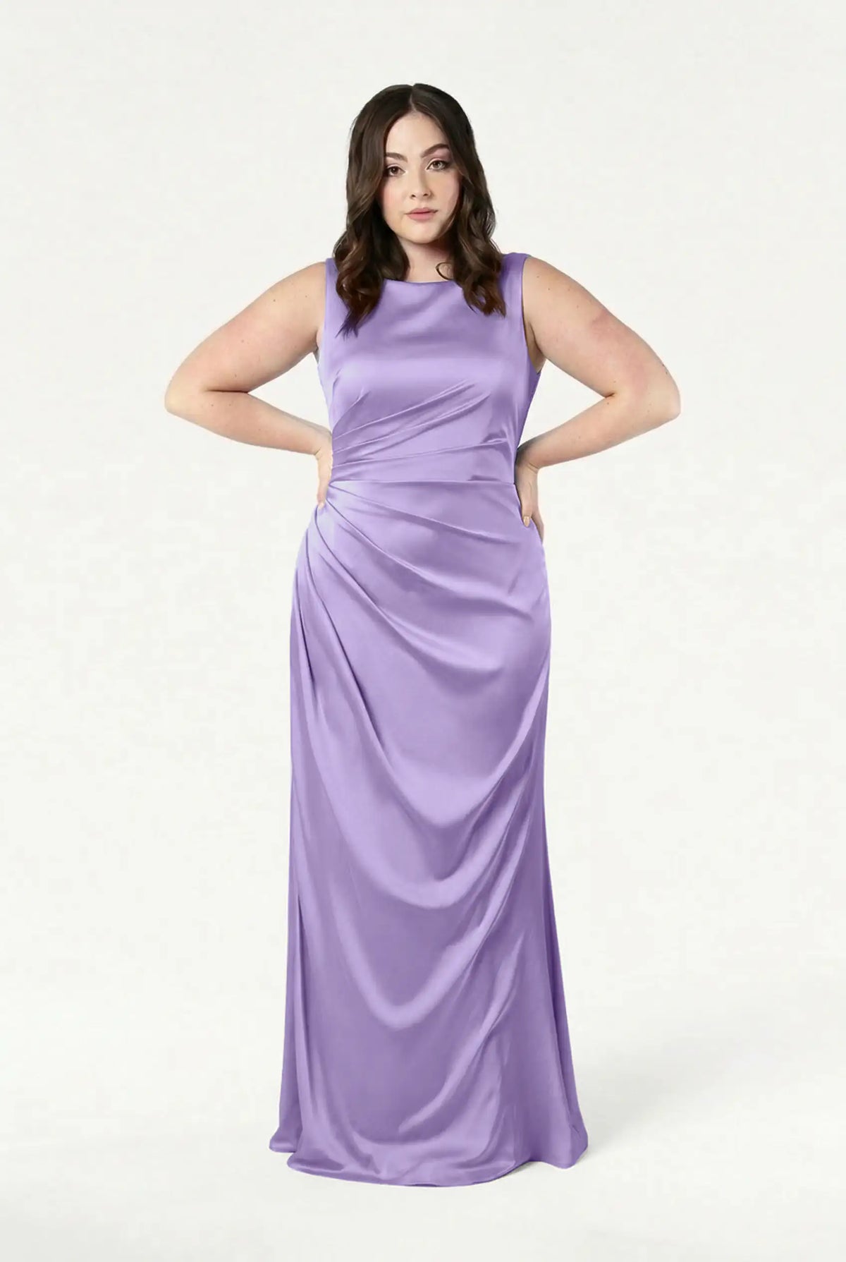 A woman with wavy brown hair stands with hands on hips, wearing the TH&TH Nala Bridesmaid Dress in Violet Satin, featuring Grecian-inspired pleating and draping—perfect for modern bridal parties—against a plain white background.