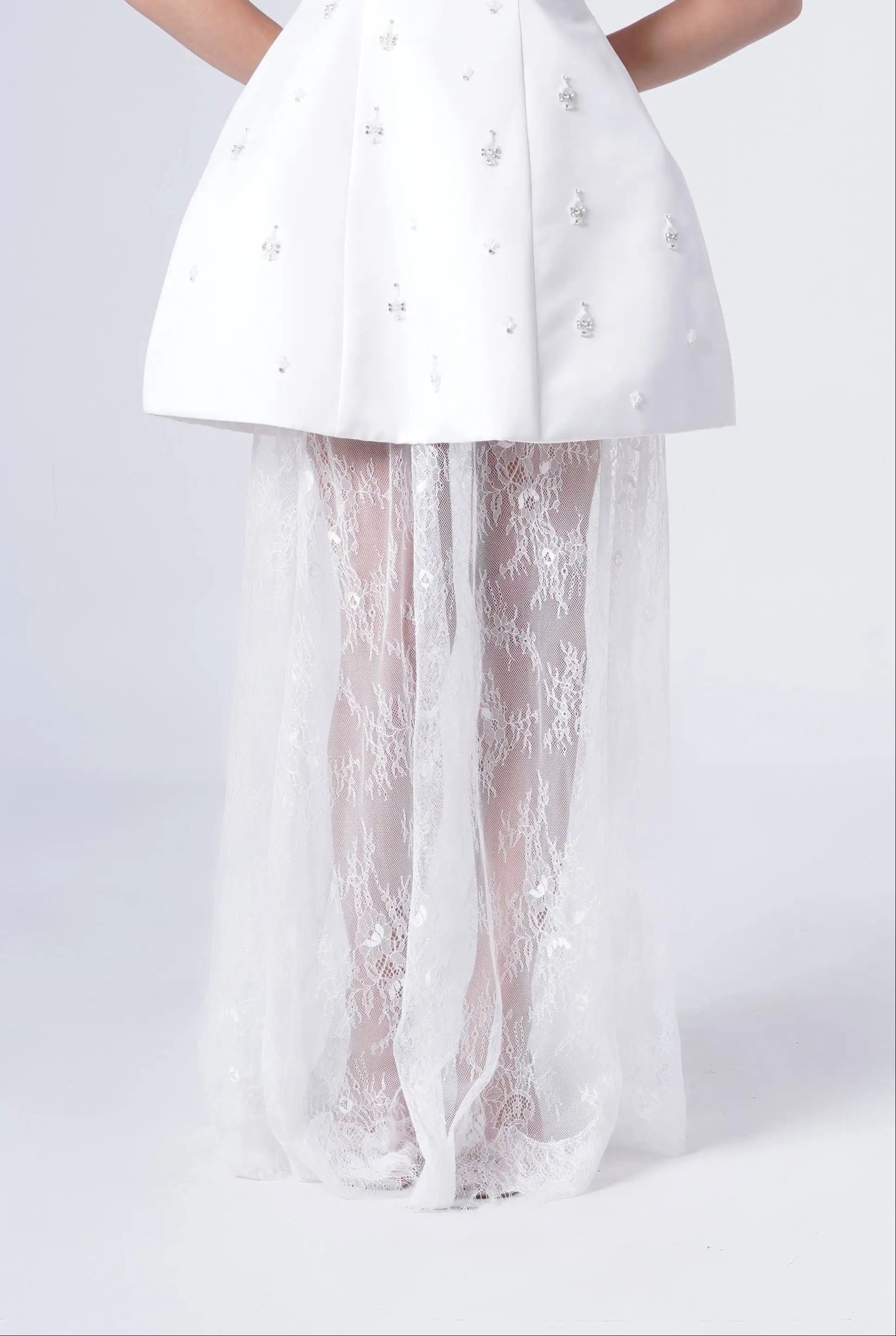 A person wears the TH&TH Nicholl Bridal Skirt in Ivory Chantilly Lace, featuring a short, structured silhouette with delicate embellishments and a floor-length Chantilly lace overlay. Only the lower body is visible against a plain background.