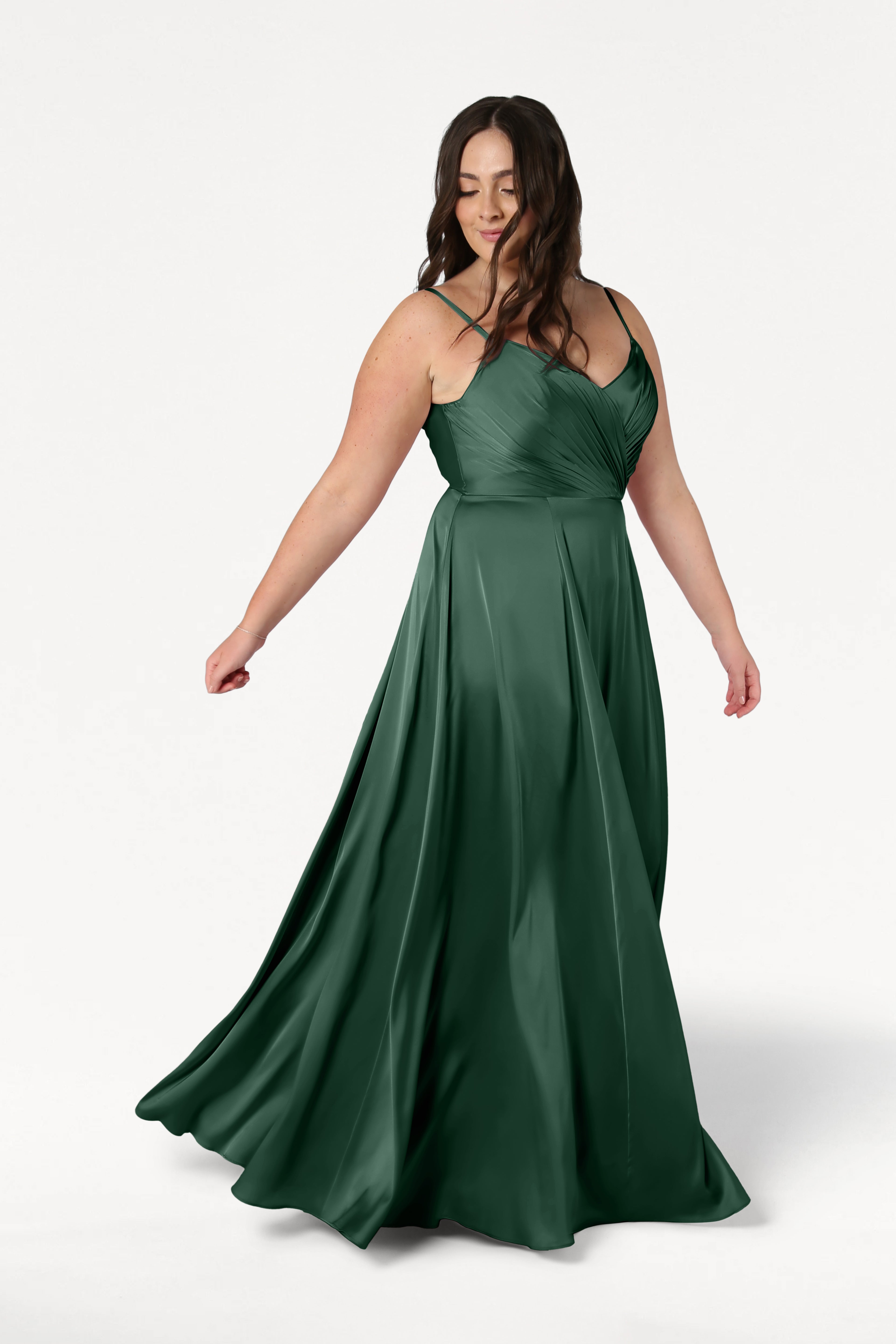 A woman wearing the TH&TH Isla Bridesmaid Dress in Olive Grove Satin—an elegant dress with a V-neckline, spaghetti straps, pleated bodice, and a flowing A-line skirt.