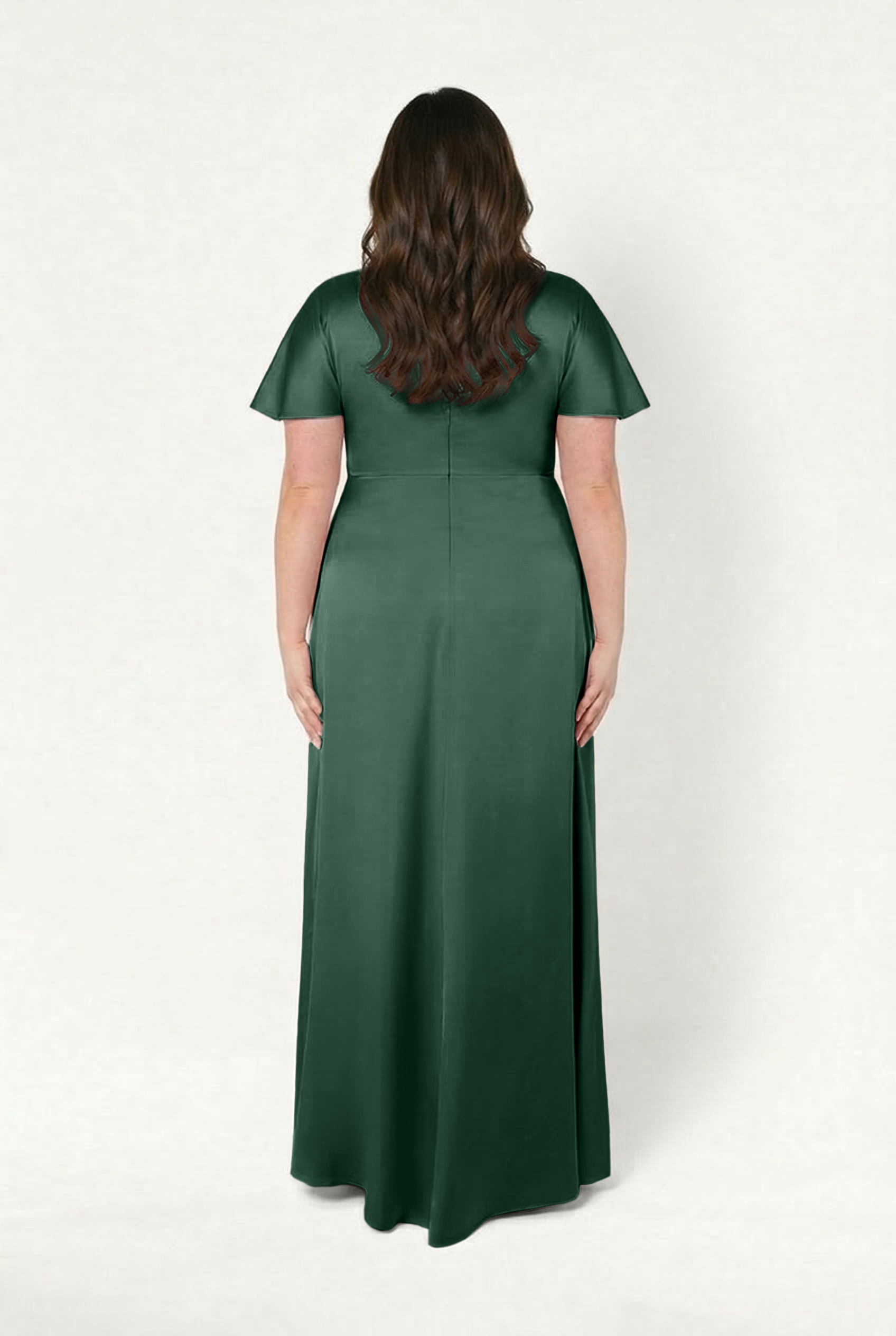 A woman with long brown wavy hair faces away, wearing the TH&TH Camilla Bridesmaid Dress in Olive Grove Satin—a floor-length, short-sleeve, size-inclusive gown—against a plain white background.