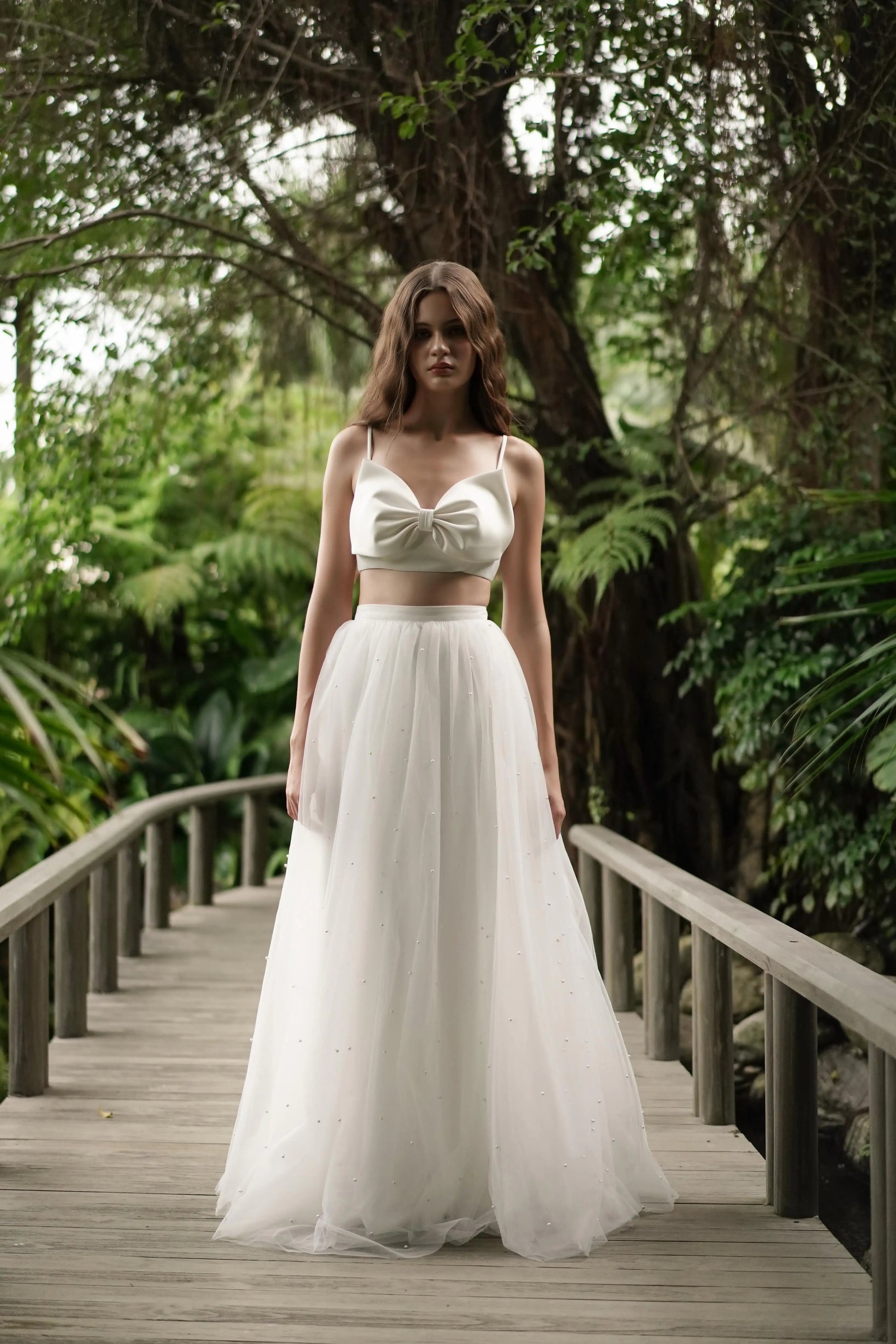 Woman in a white dress standing on a wooden bridge in a forest setting