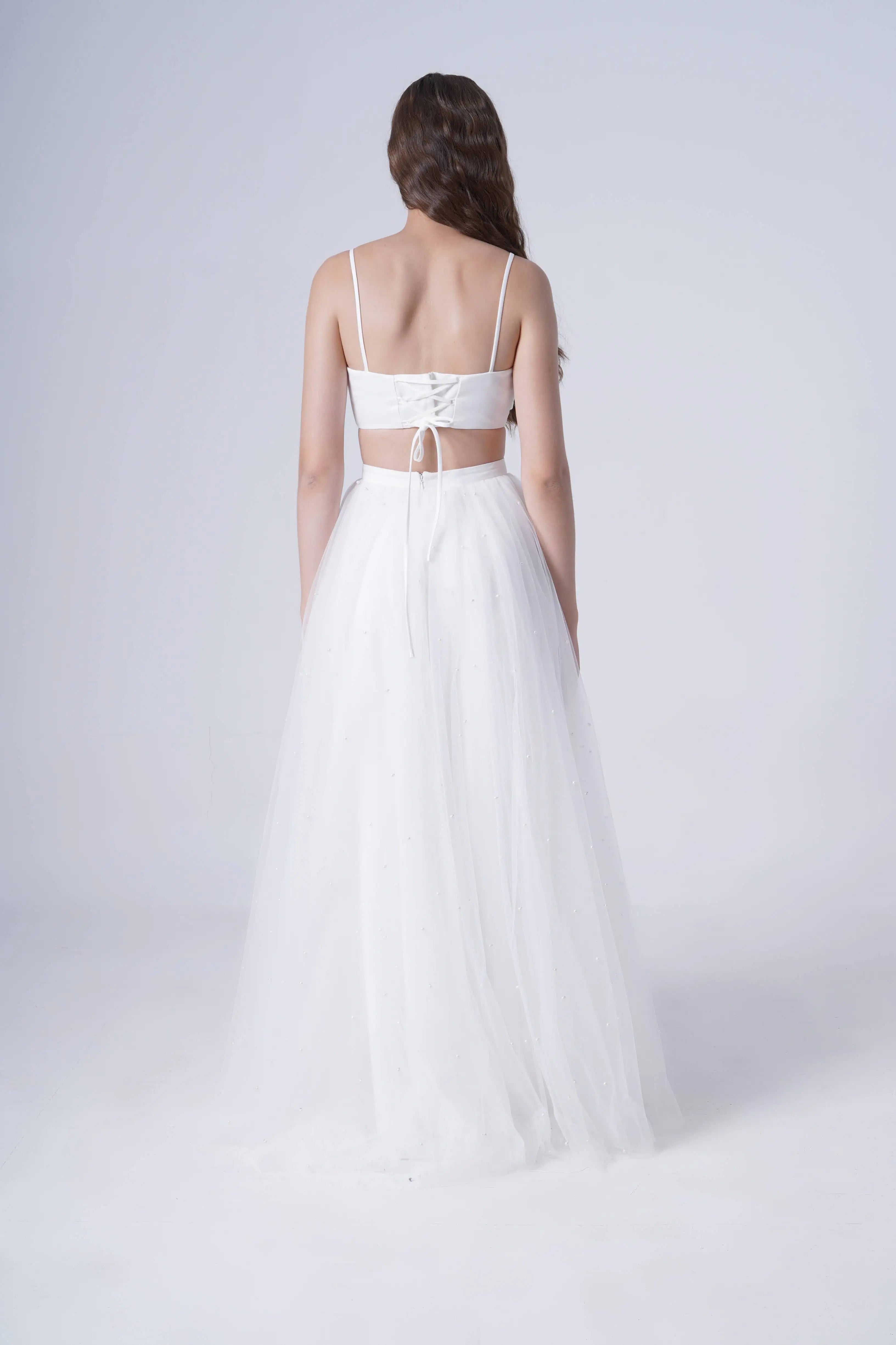 Woman wearing a white wedding dress with a sheer overlay on a light gray background