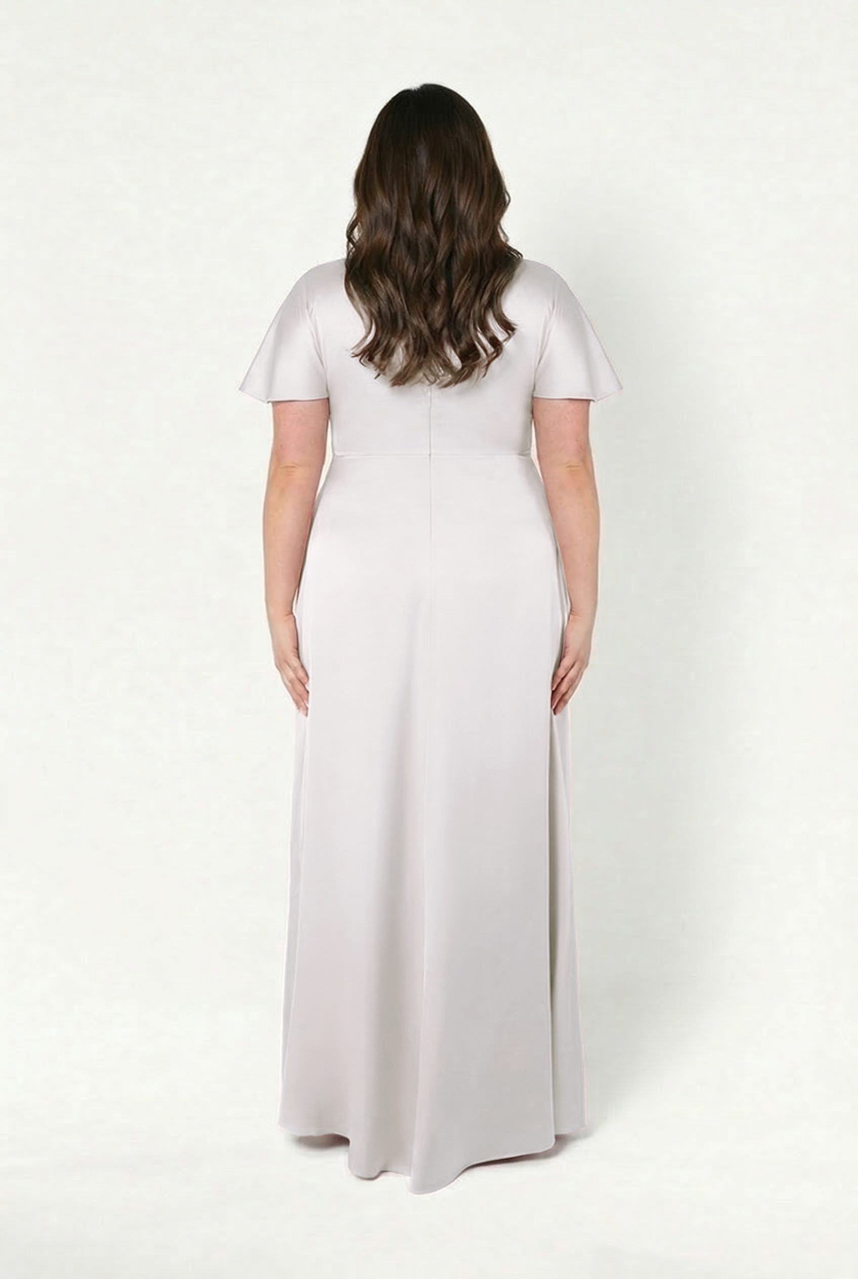 A woman with long wavy brown hair stands with her back to the camera, wearing the TH&TH Camilla Bridesmaid Dress in Oyster Satin, a floor-length, short-sleeve gown, against a plain white background.