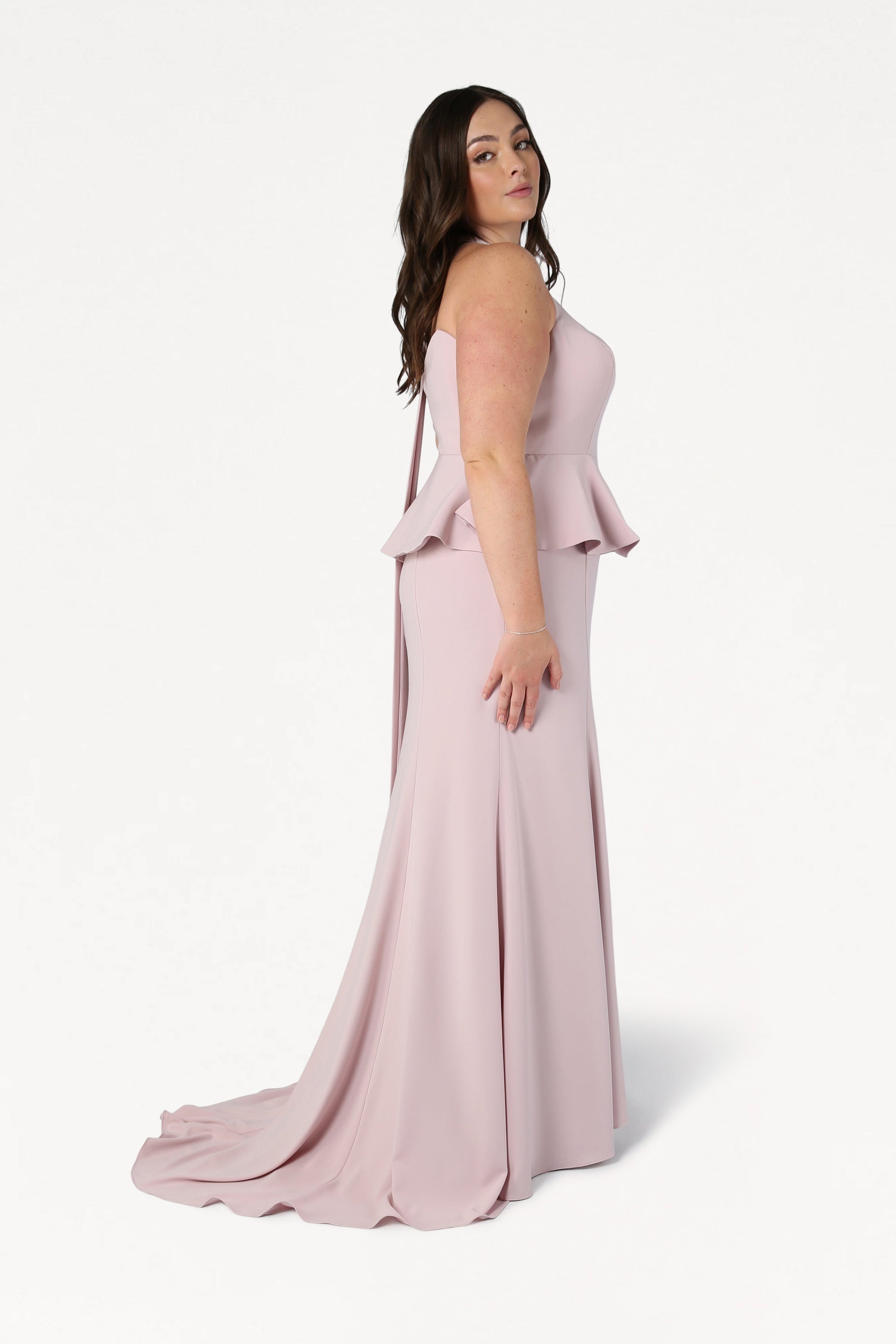 A woman with long brown hair models the TH&TH Peony Bridesmaid Dress in Smoked Blush, a size-inclusive, strapless gown with a fitted bodice and floor-length flared skirt, against a plain white background.