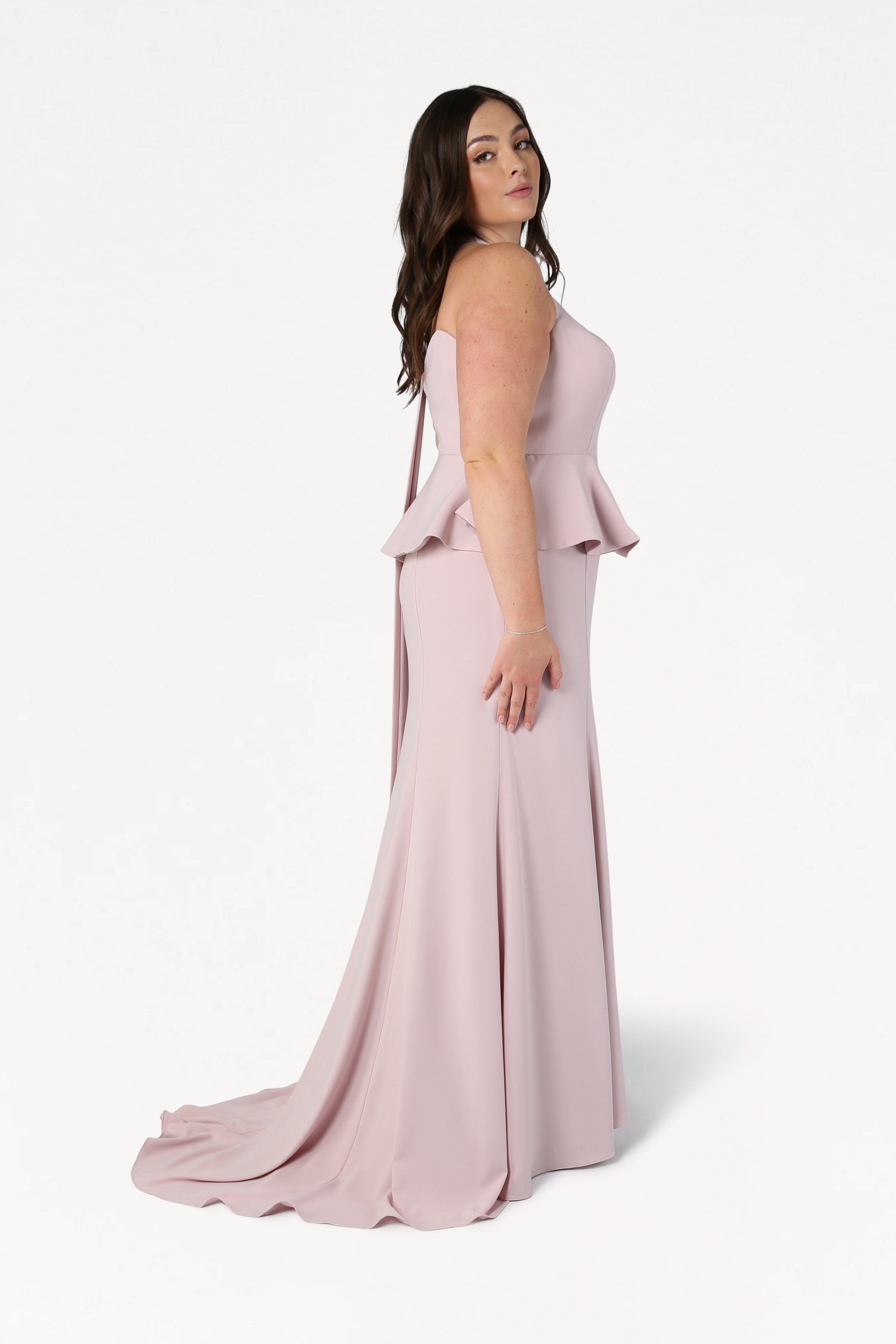 A woman with long brown hair models the TH&TH Peony Bridesmaid Dress in Smoked Blush, a size-inclusive, strapless gown with a fitted bodice and floor-length flared skirt, against a plain white background.