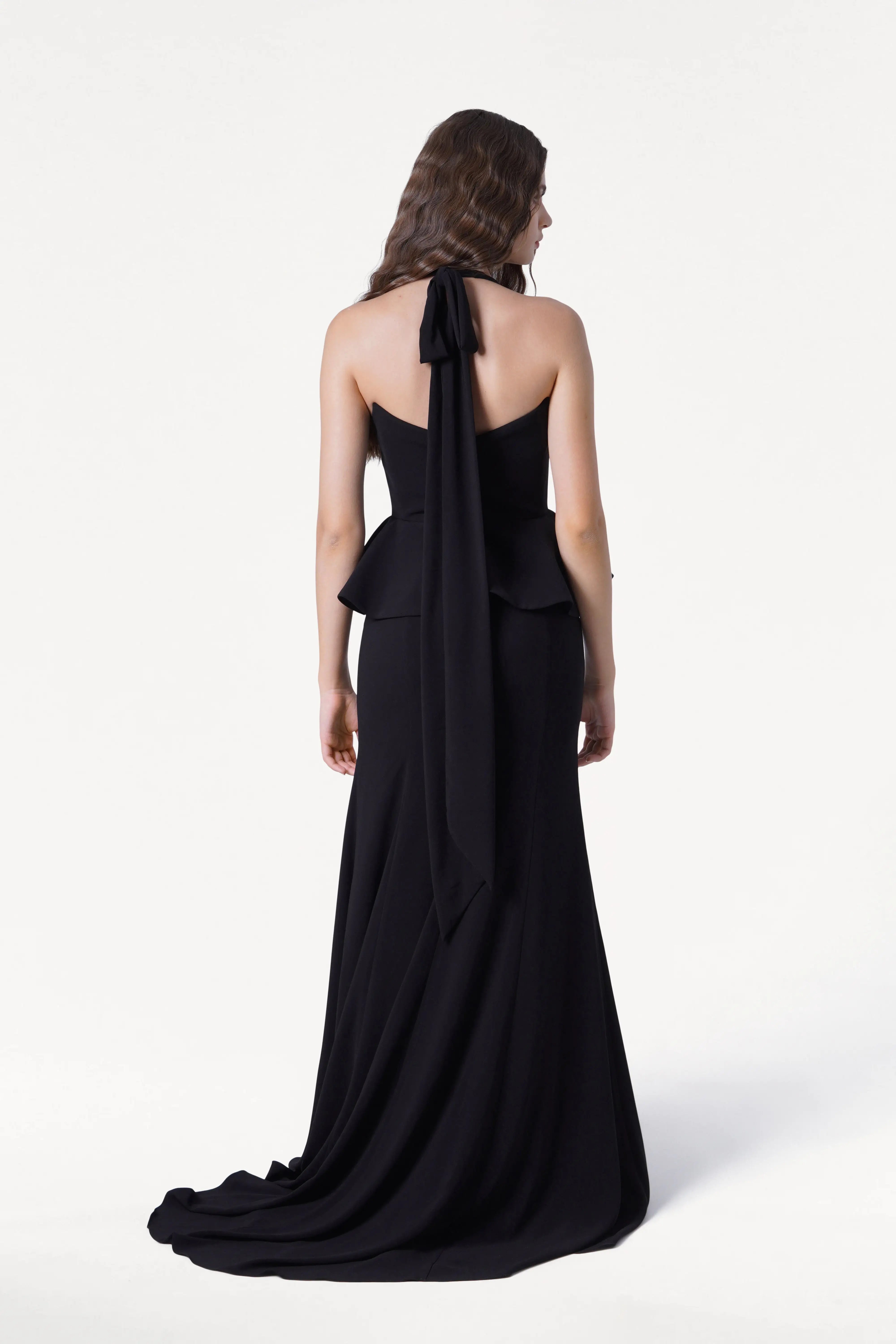 Woman wearing a black halter neck gown with a long train on a white background